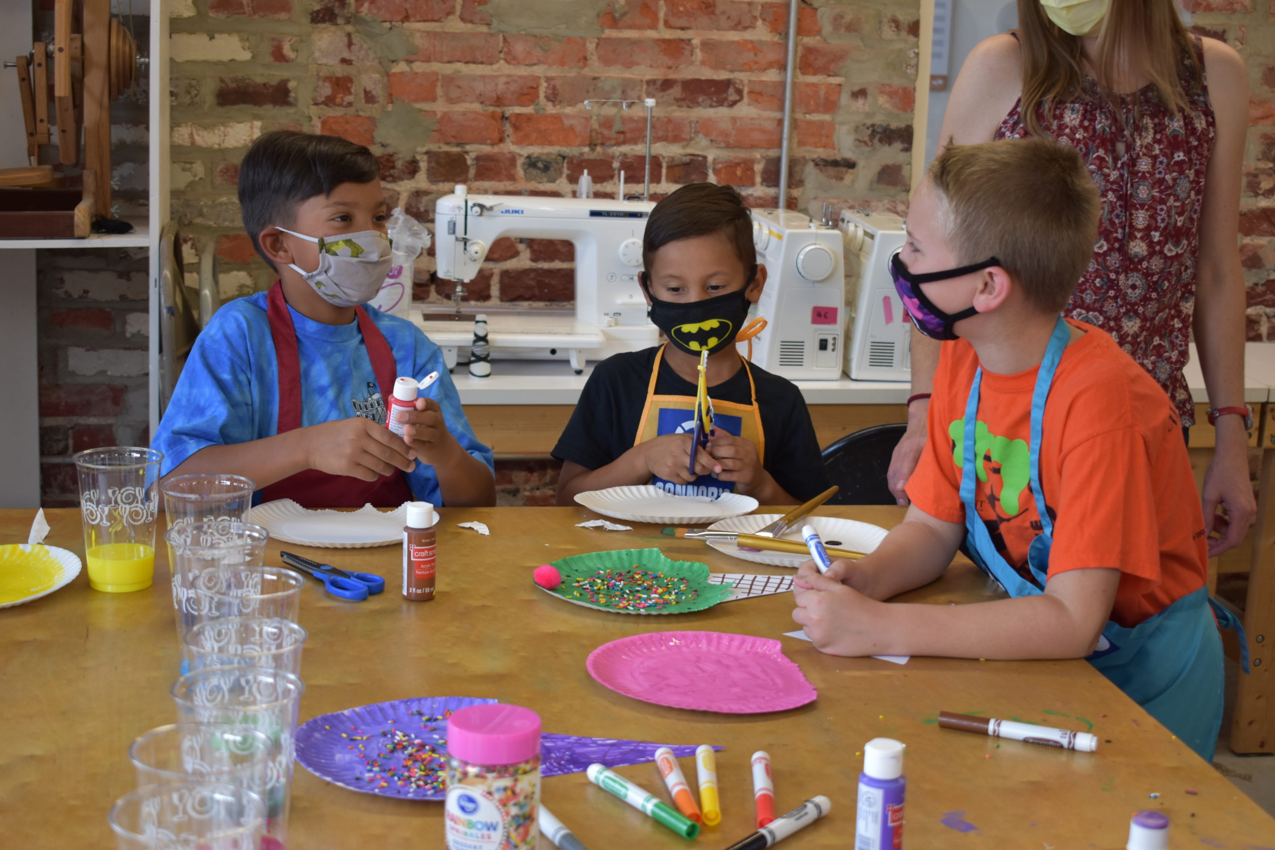 Three children at a table in an art studio painting paper plates