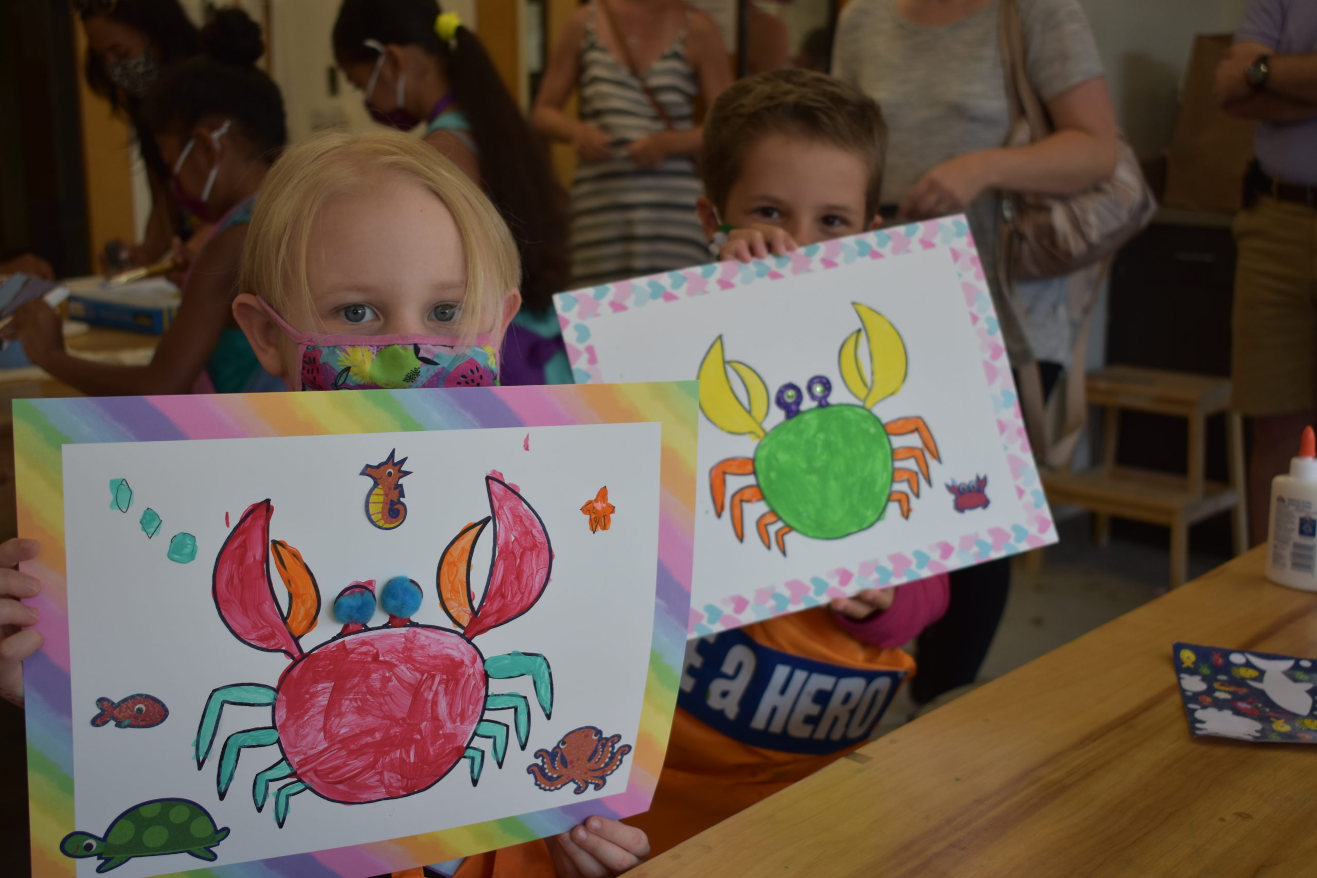 Two children holding up their paintings of crabs