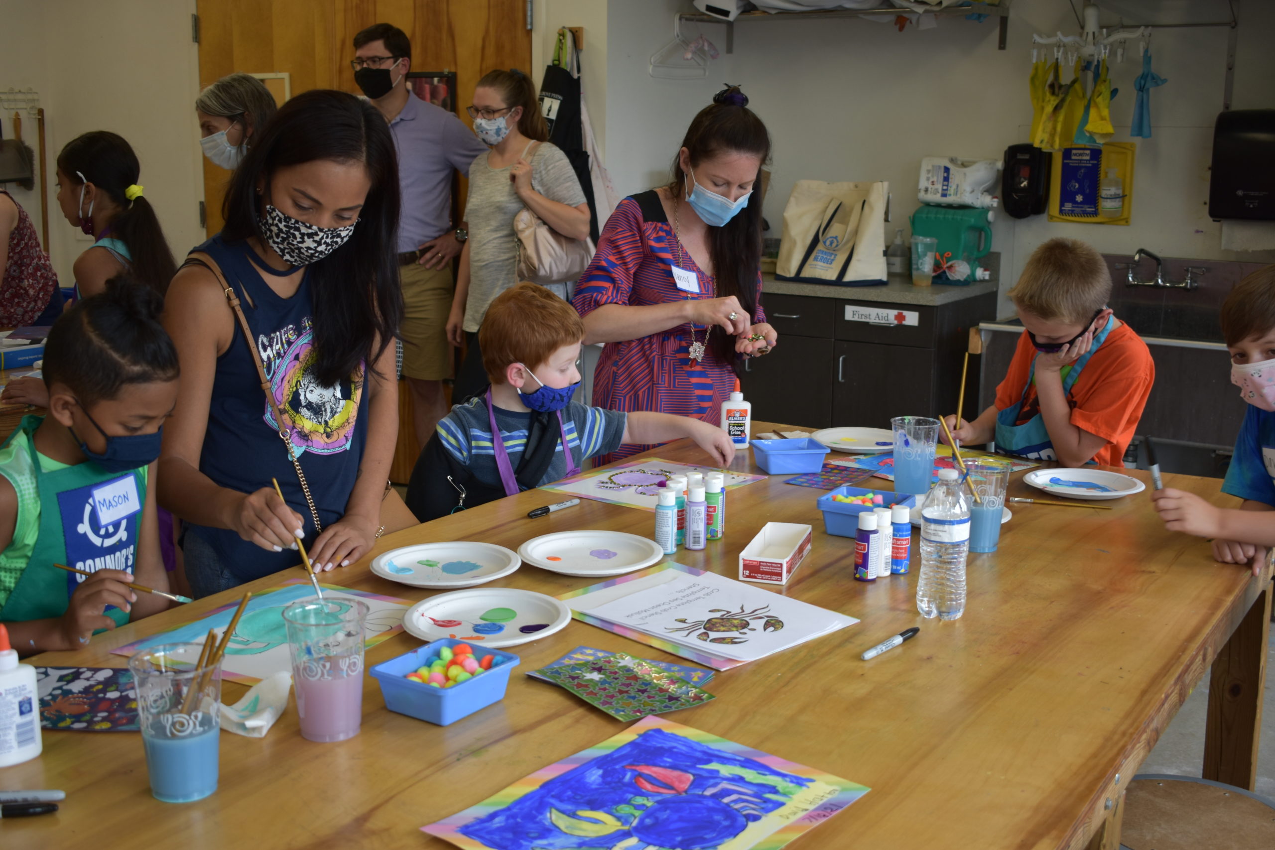Two adults and four child at a table painting in an art studio