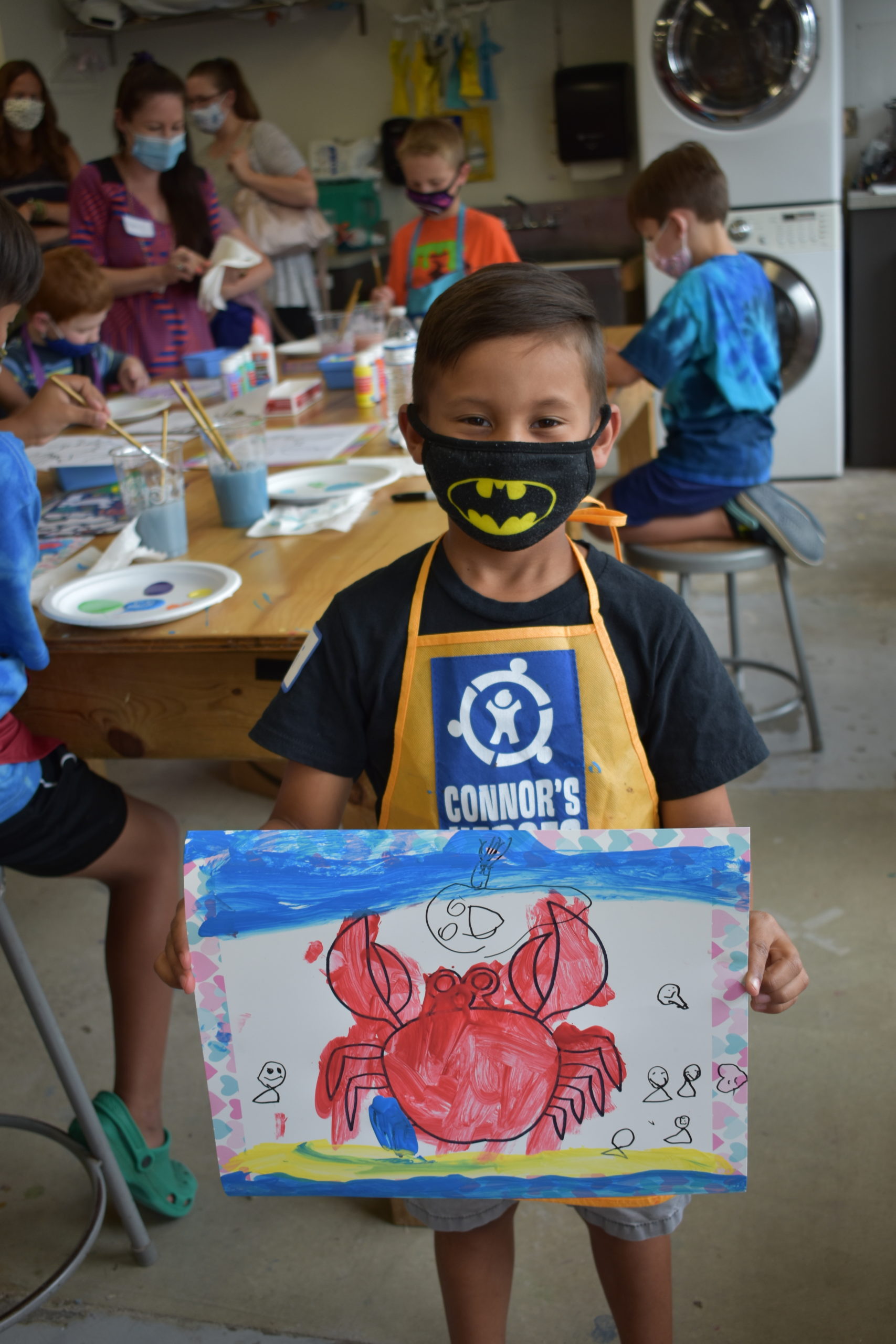 A child wearing a mask holding up a painting of a crab
