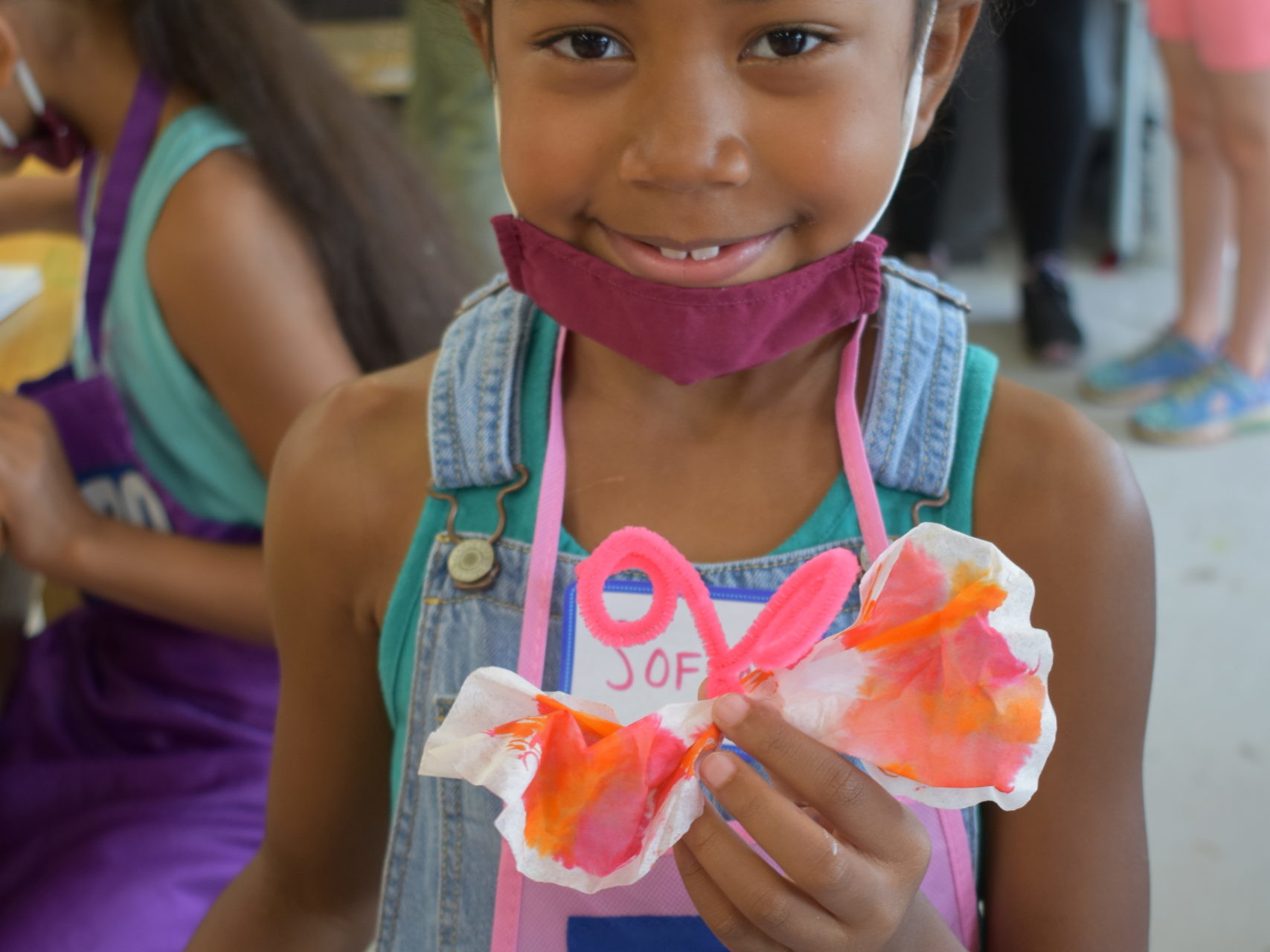 Image a child looking into the camera holding a paper butterfly
