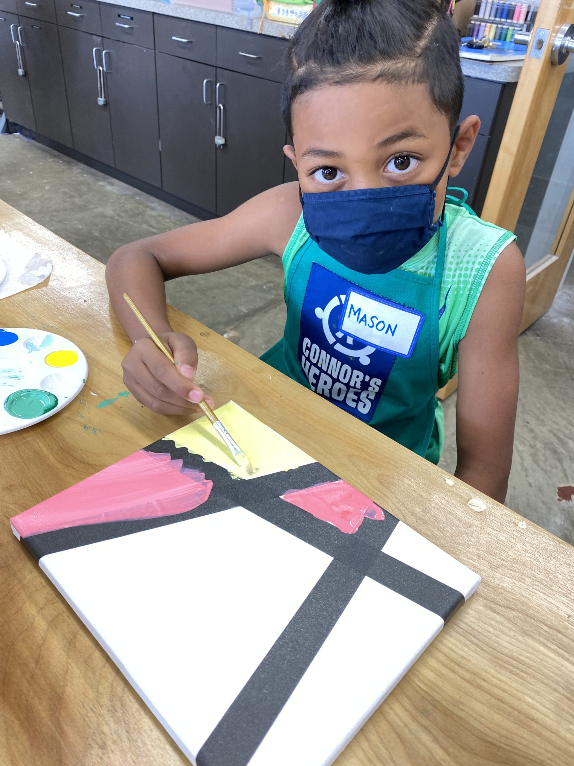 Image a child wearing a mask and painting a small canvas
