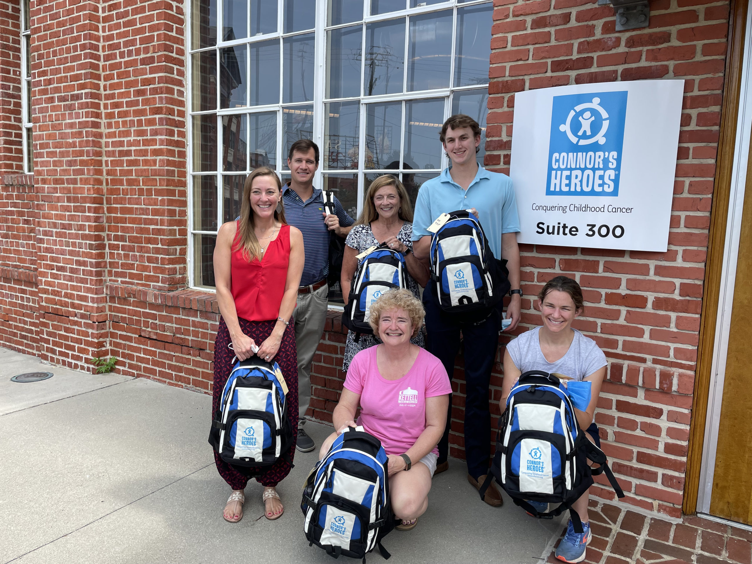 Image A group of six people holding backpacks standing outside of the Connors Heroes office