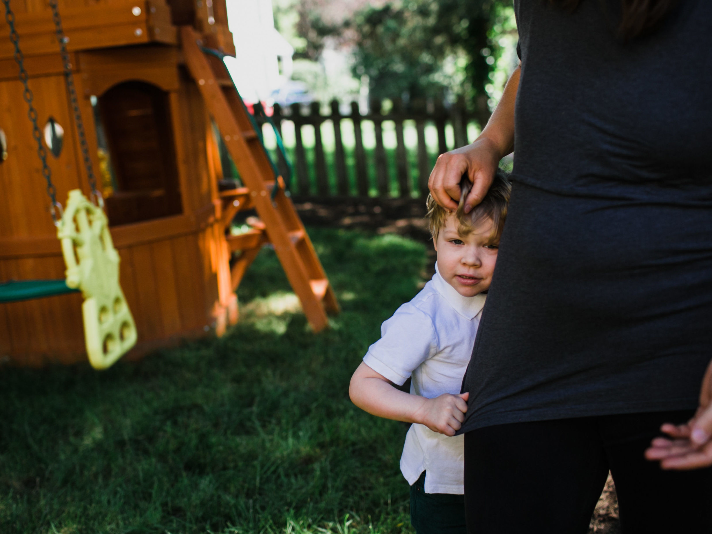 Image child hugging the leg of his mom standing in their backyard