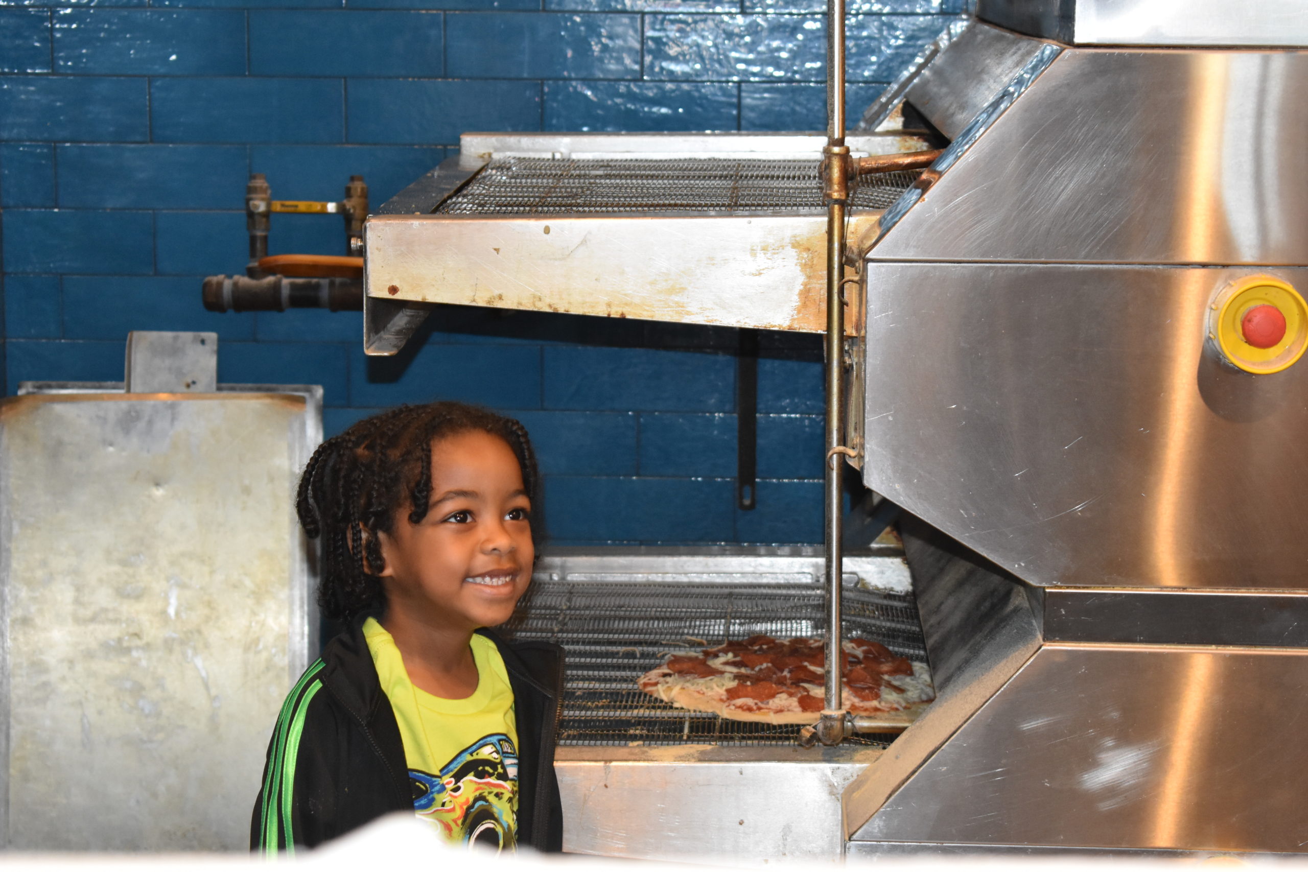 Image boy standing in a restaurant kitchen watching his pizza bake in an over