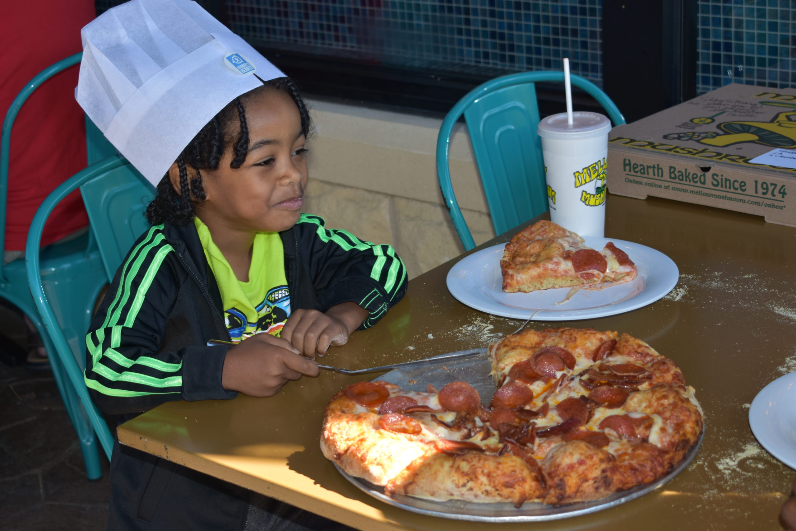 Image boy wearing a chef hat and eating a pizza