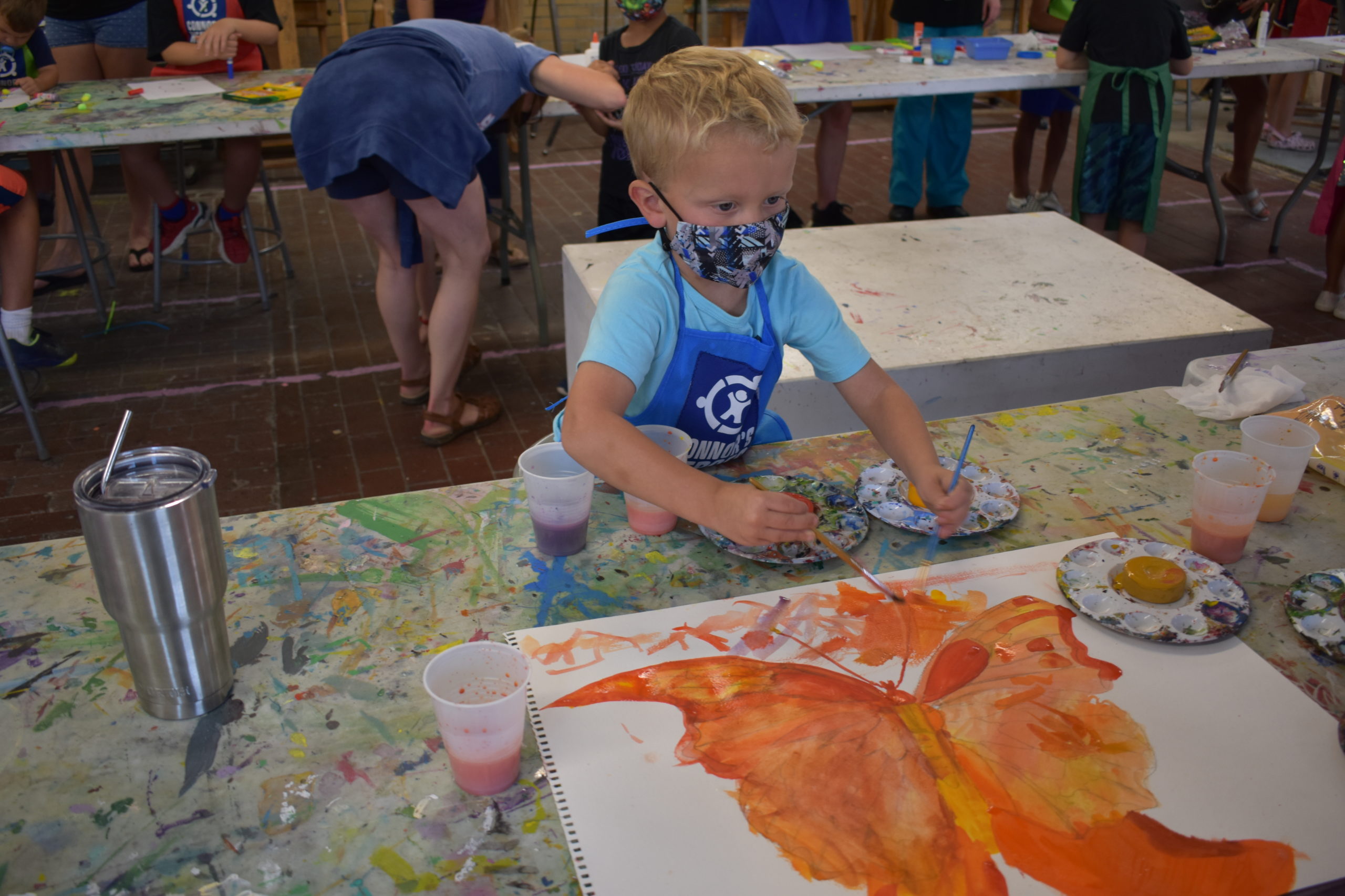 Image a boy in an art studio painting a picture of an orange butterfly