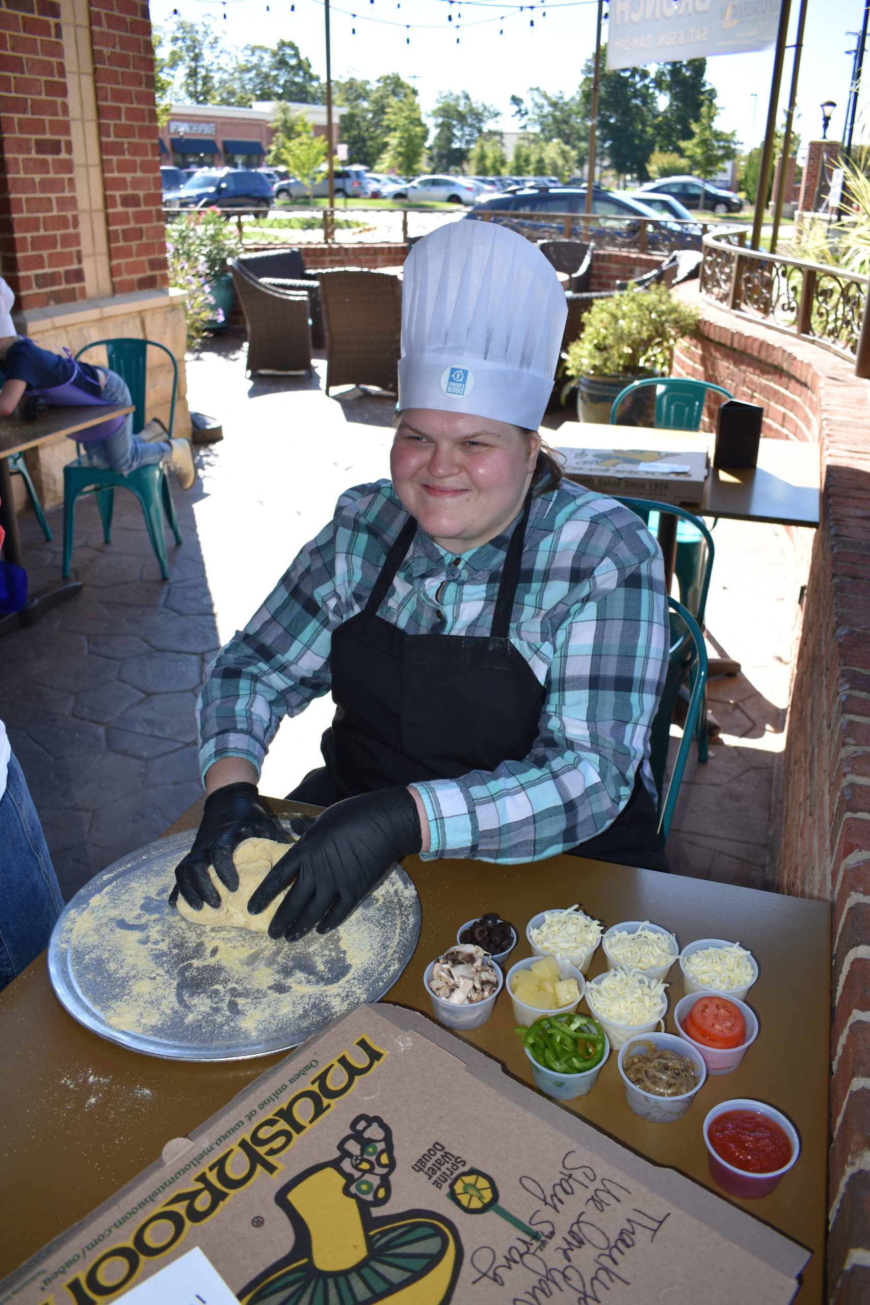 Image a girl wearing a chef hat and rolling pizza dough