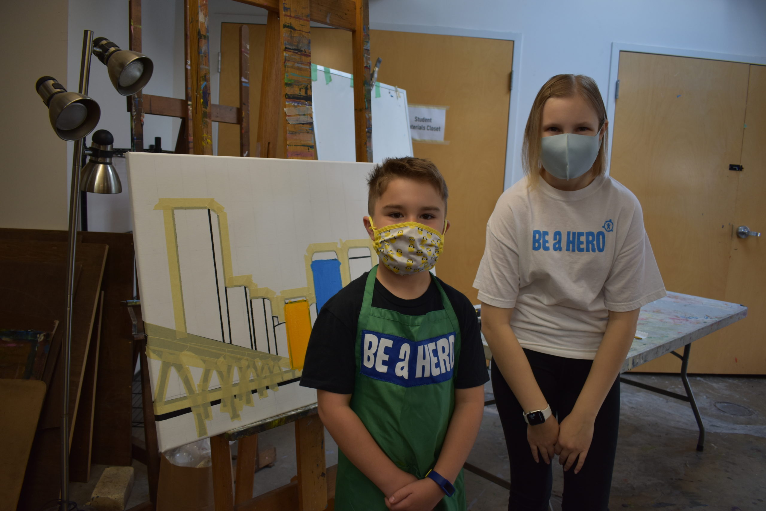 Image two children in an art studio wearing shirts that say Be A Hero