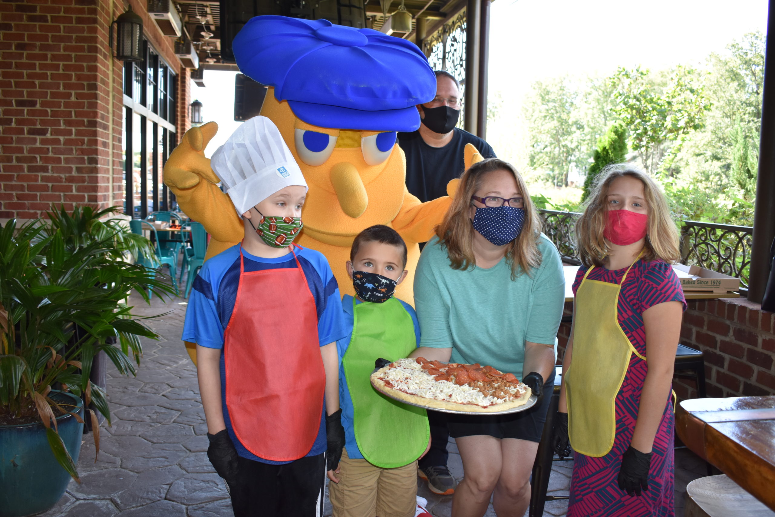 Image a family standing with a person wearing a mushroom costume and holding a pizza