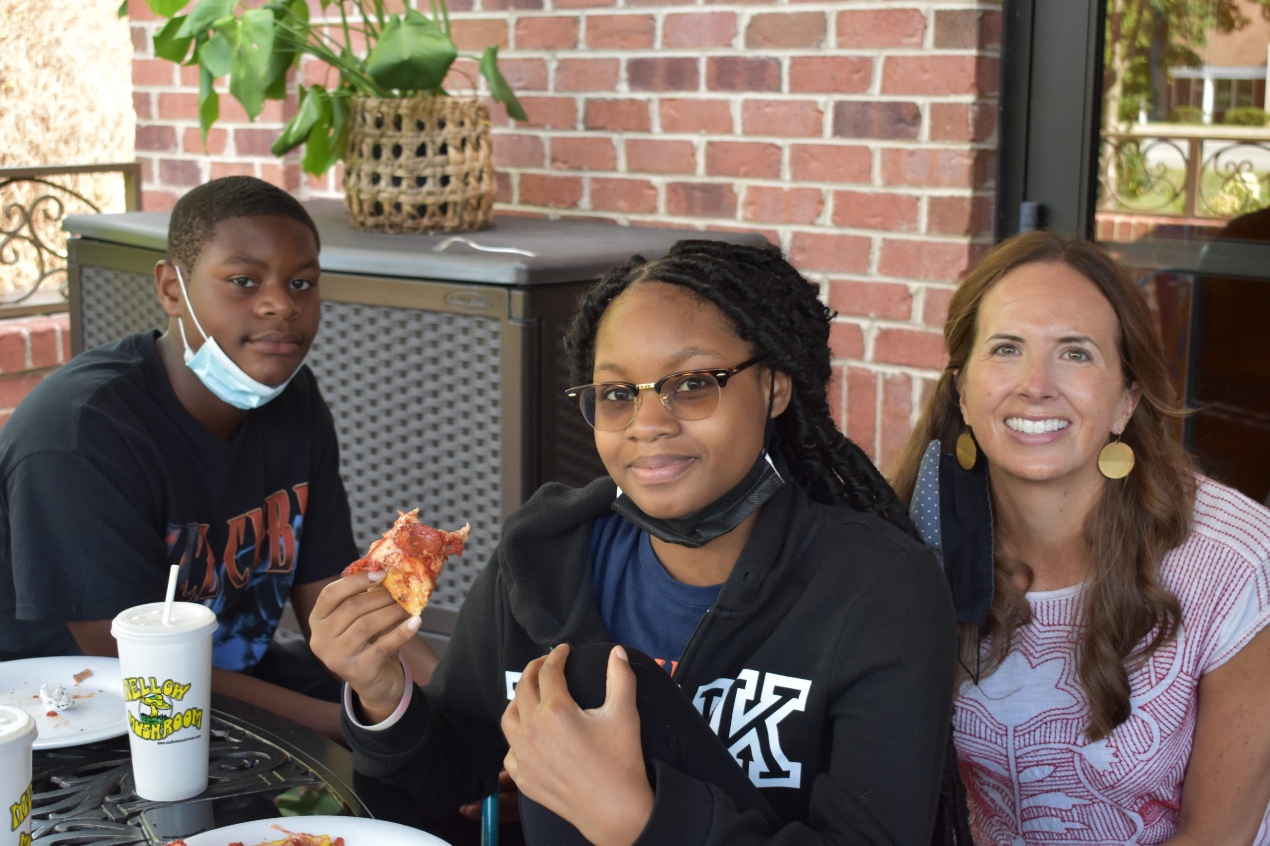 Image two teenagers and an adult sitting together eating pizza