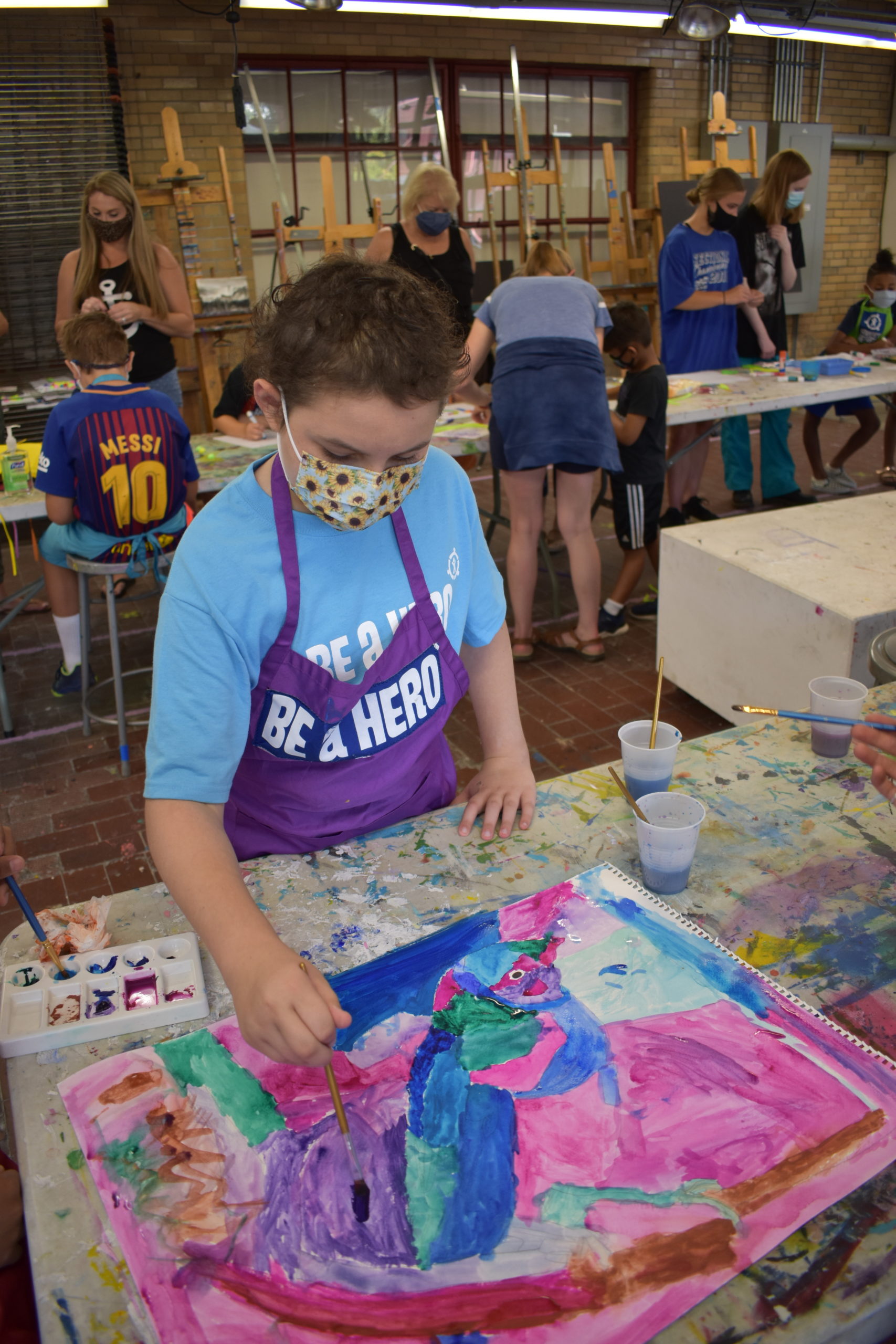 Image girl wearing a apron saying Be A Hero and painting a picture in an art studio