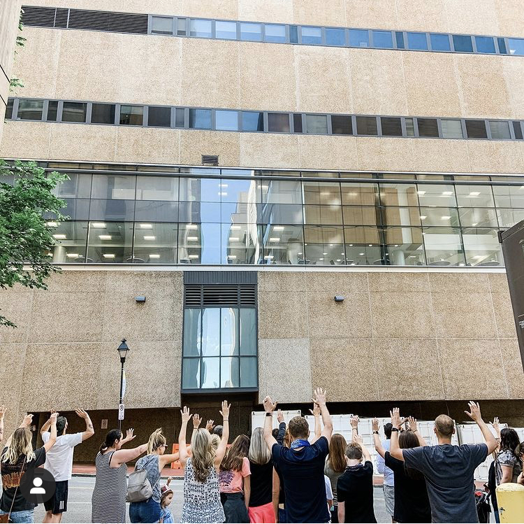 Image a group of people standing outside of a building with their hands raised up in prayer