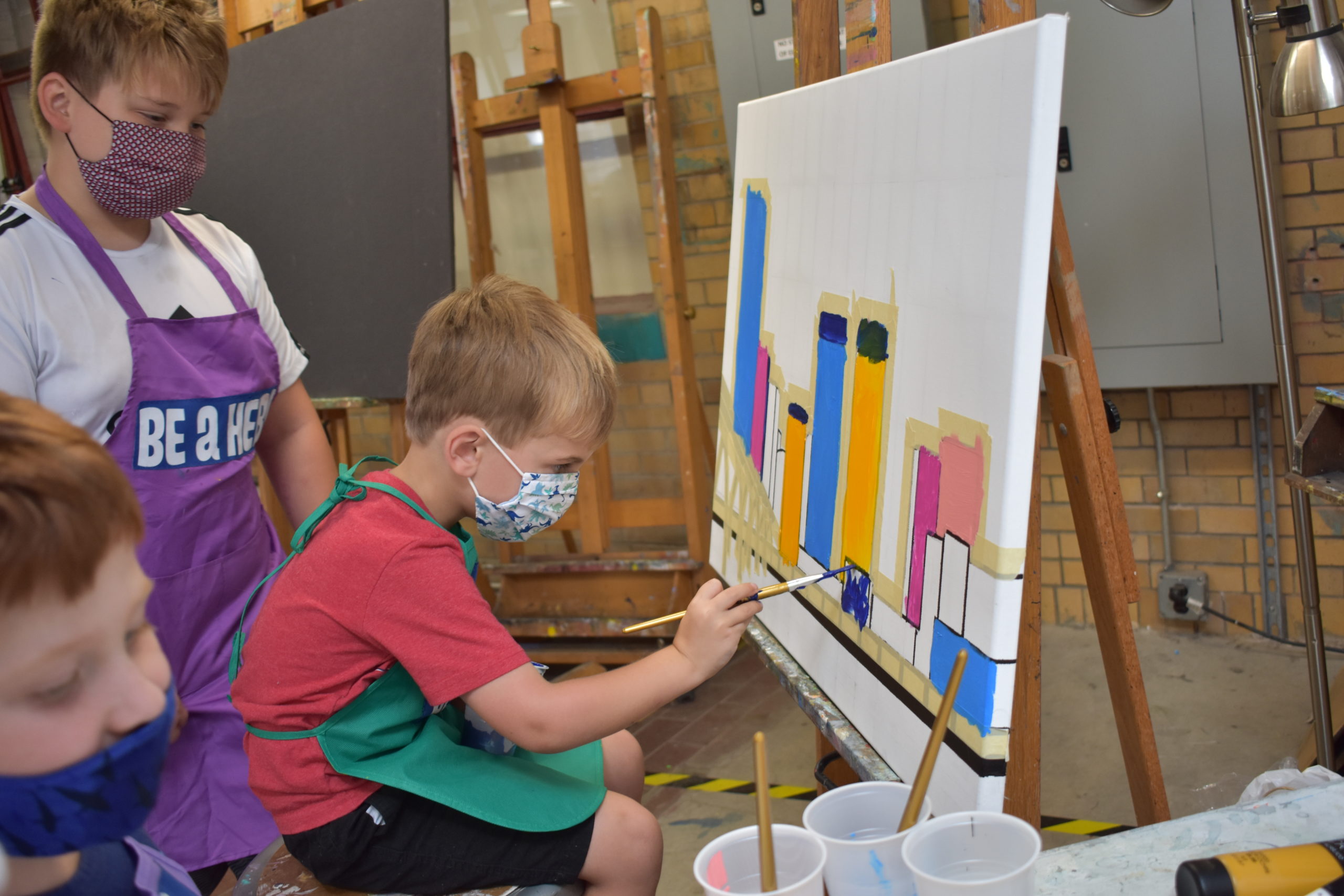 Image In an art studio three children are painting buildings on a white canvas