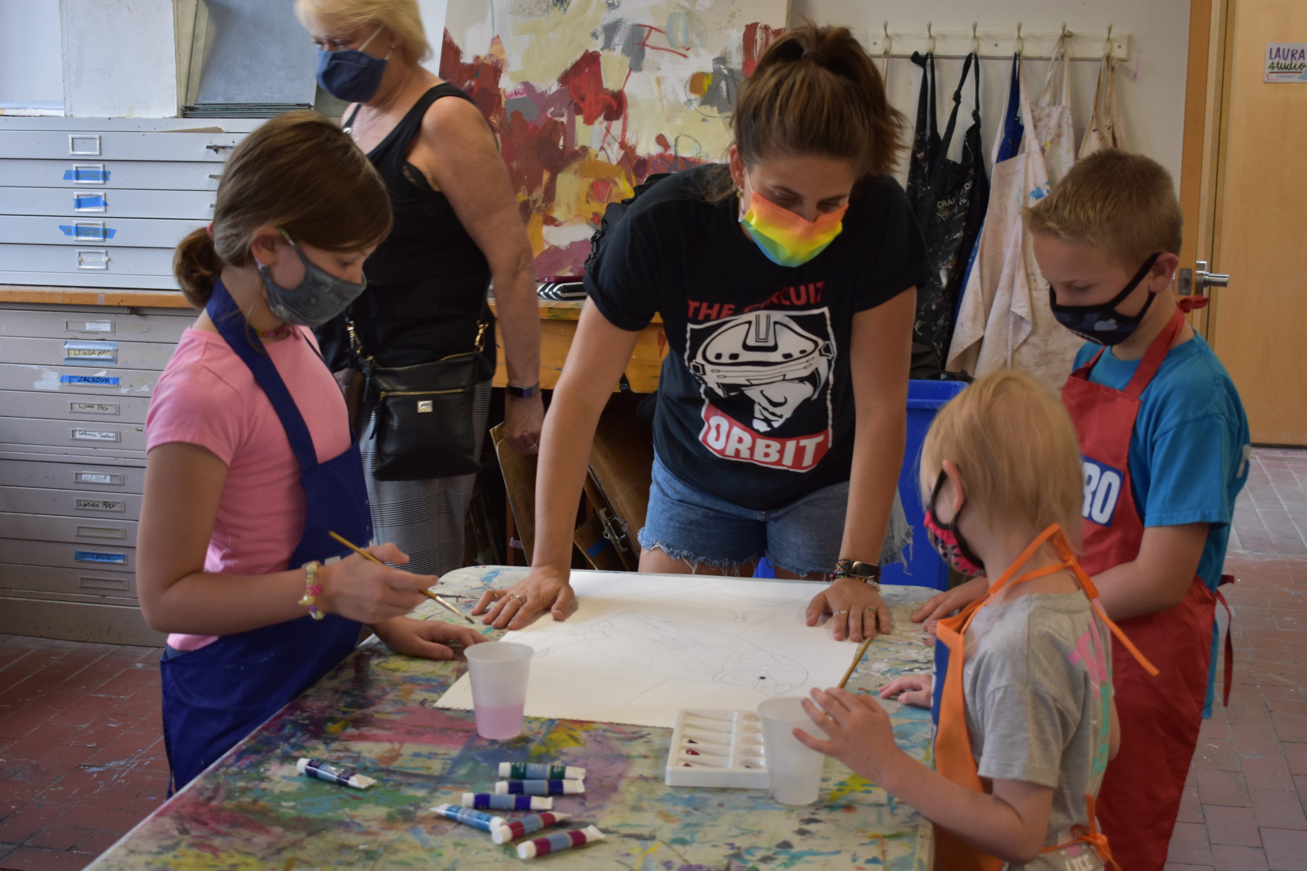 Image In an art studio an adult is helping a group of children paint a picture