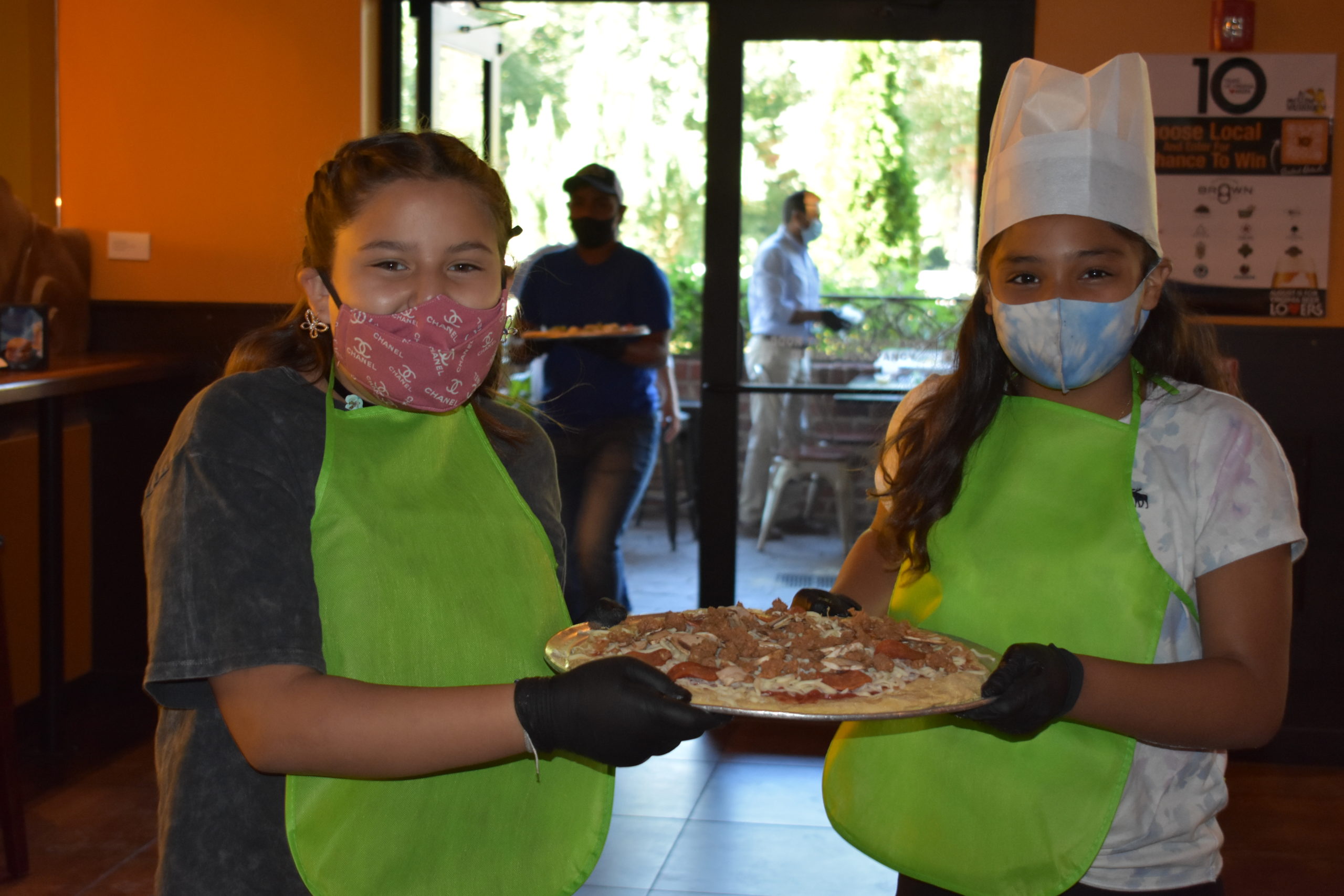 Image two children carrying a pizza into the kitchen of a restaurant