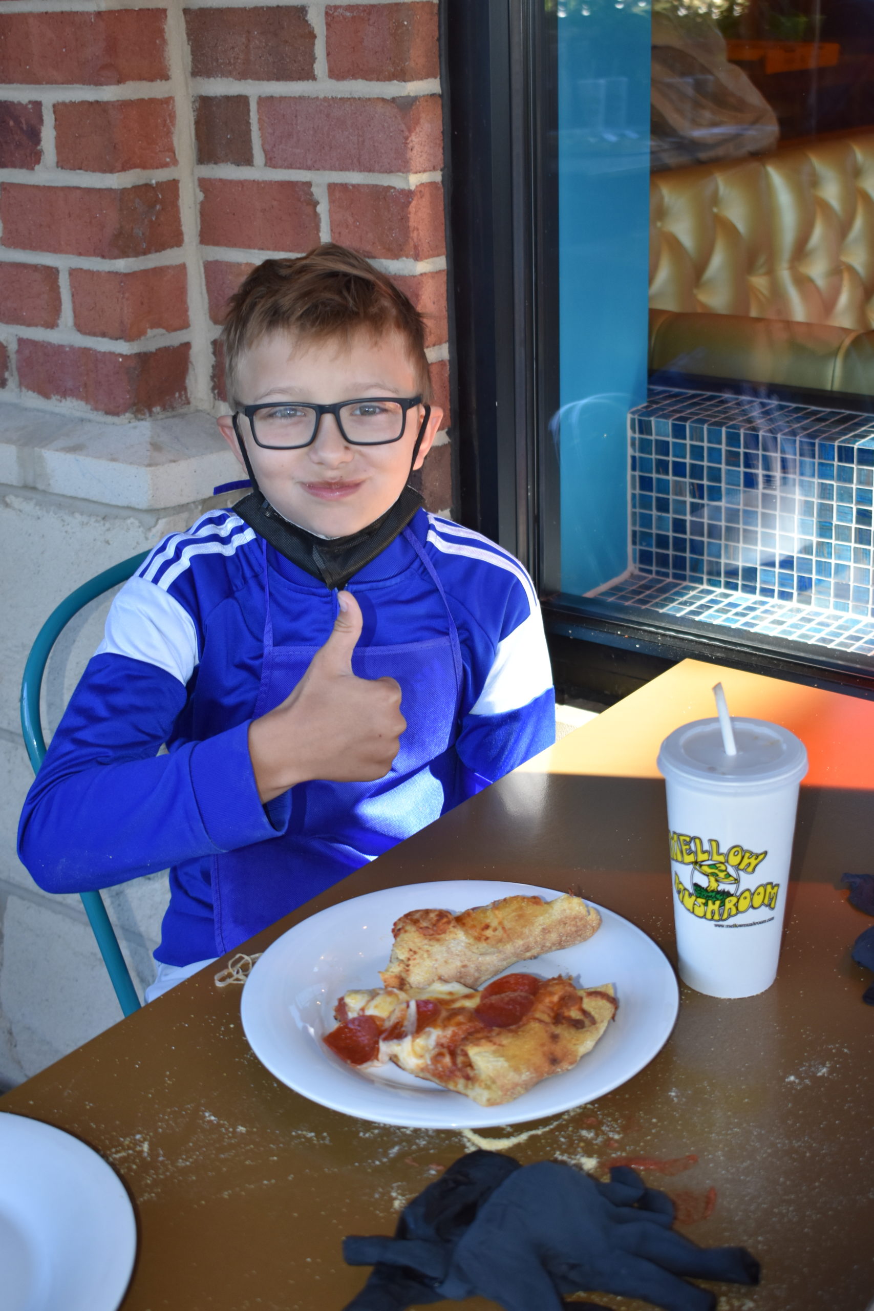 Image a boy eating pizza and giving a thumbs up with a smile