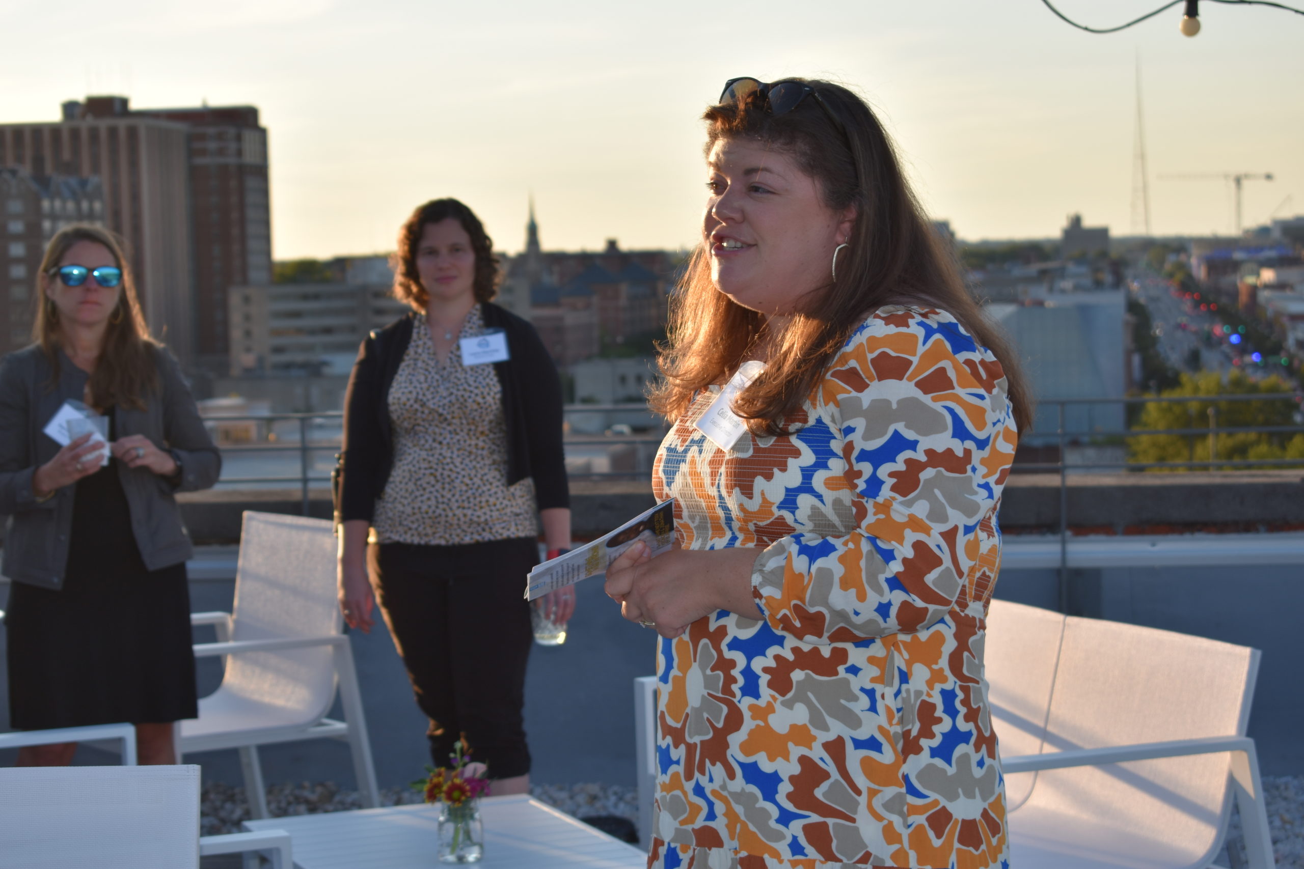 a person speaking to a group of people who are standing at a rooftop overlooking Richmond Virginia