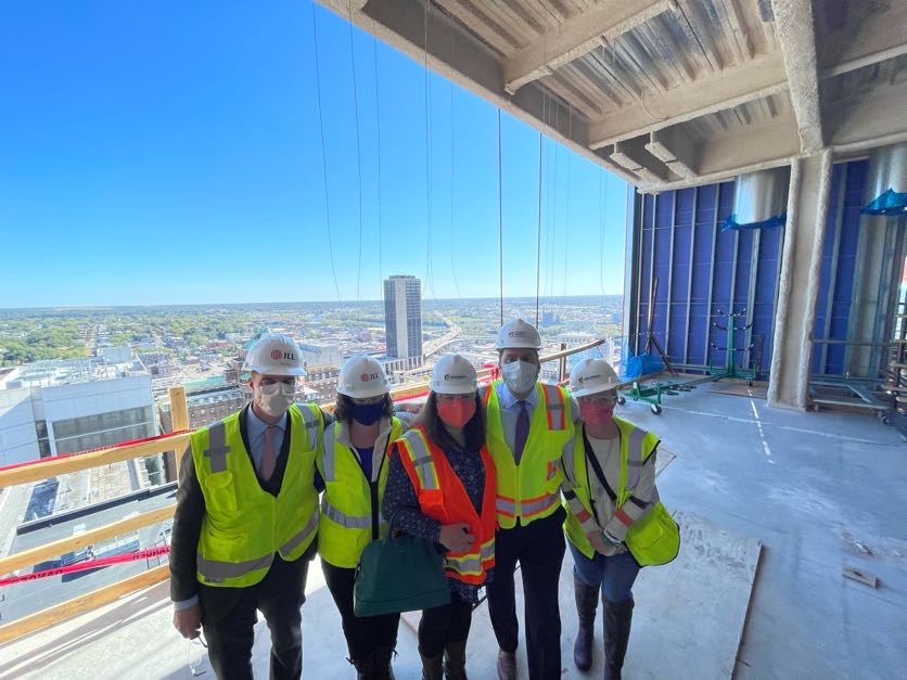 Group of people wearing yellow safety vests and hardhats standing outside on a platform overlooking the city