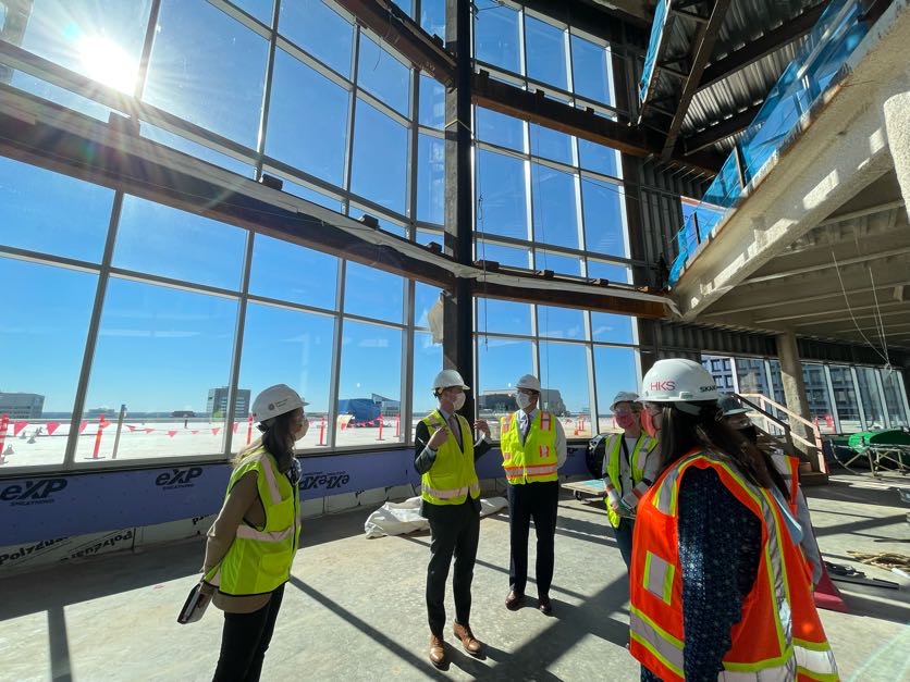 Group of people wearing yellow safety vests and hardhats standing in a large atrium under construction