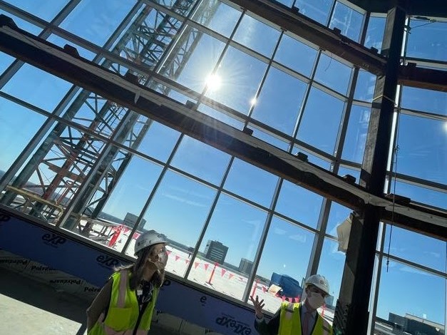 Two people wearing yellow safety vests and hardhats standing in a large atrium under construction