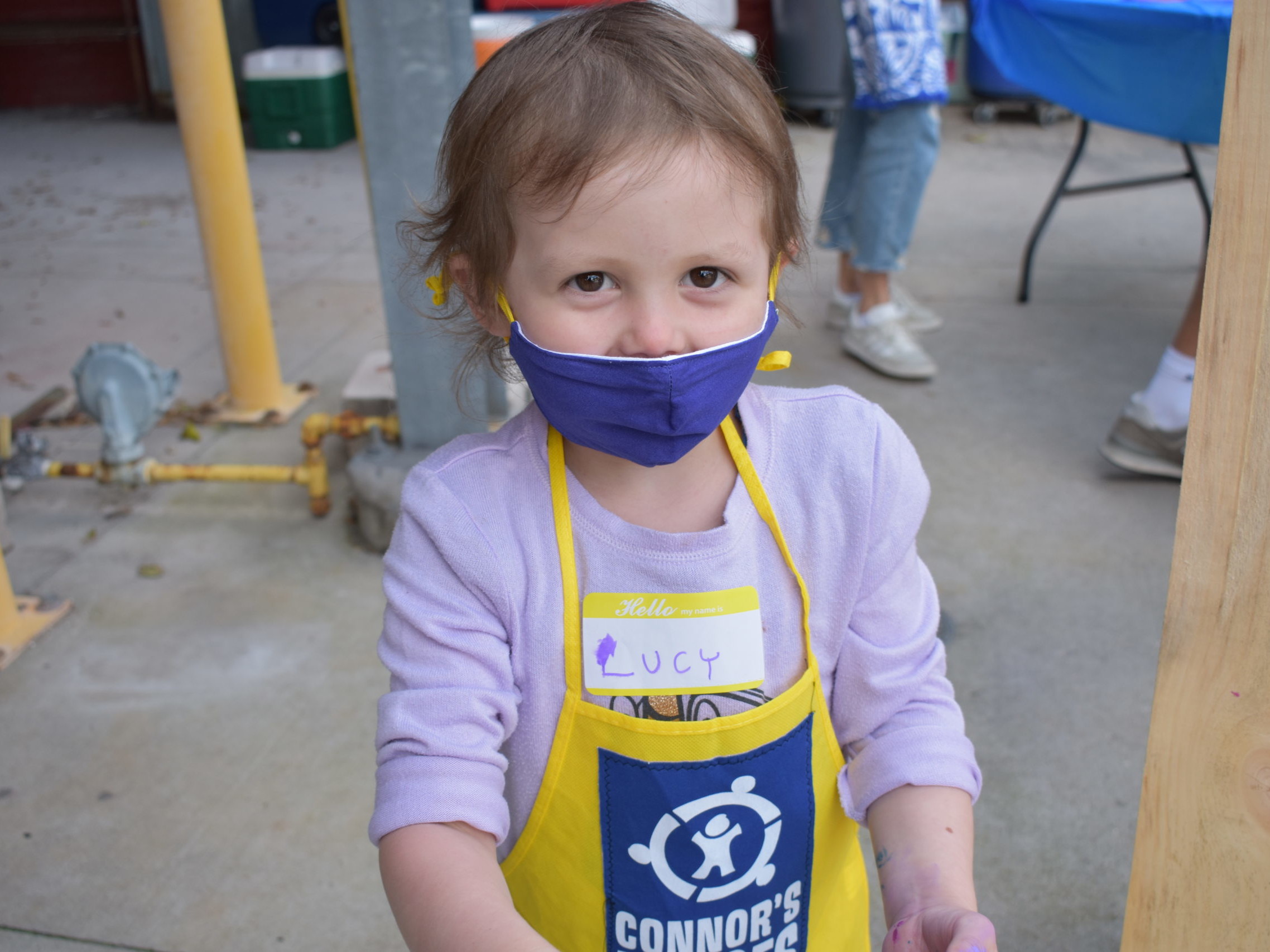 A child wearing a facemask and a yellow apron