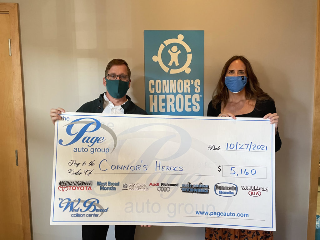 Two adults standing together holding up an oversized check from the Page Auto Group to Connors Heroes