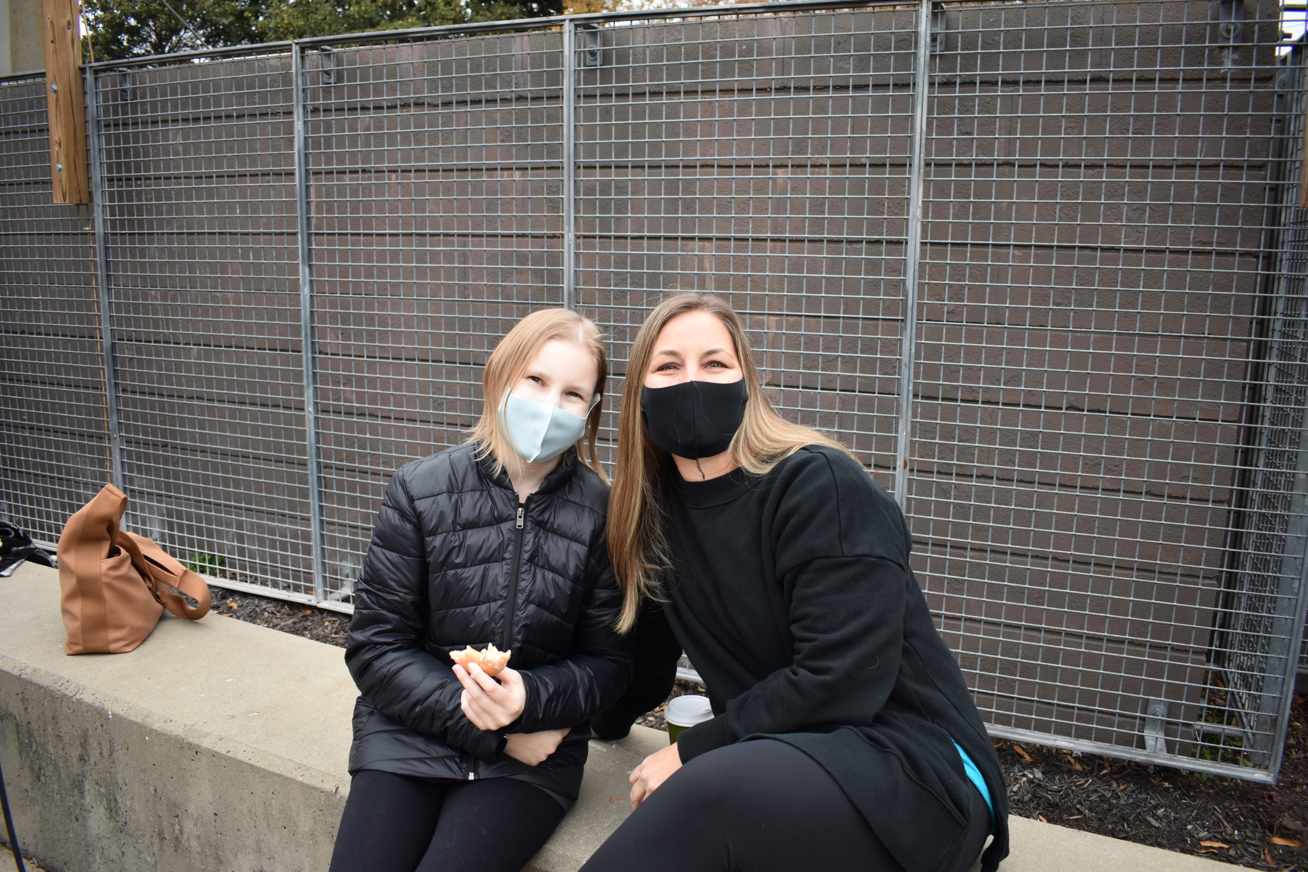A teenager and her mom wearing cloth masks and sitting in an outdoor courtyard