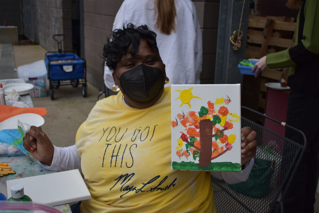 A woman wearing a mask holding up a painting of a tree