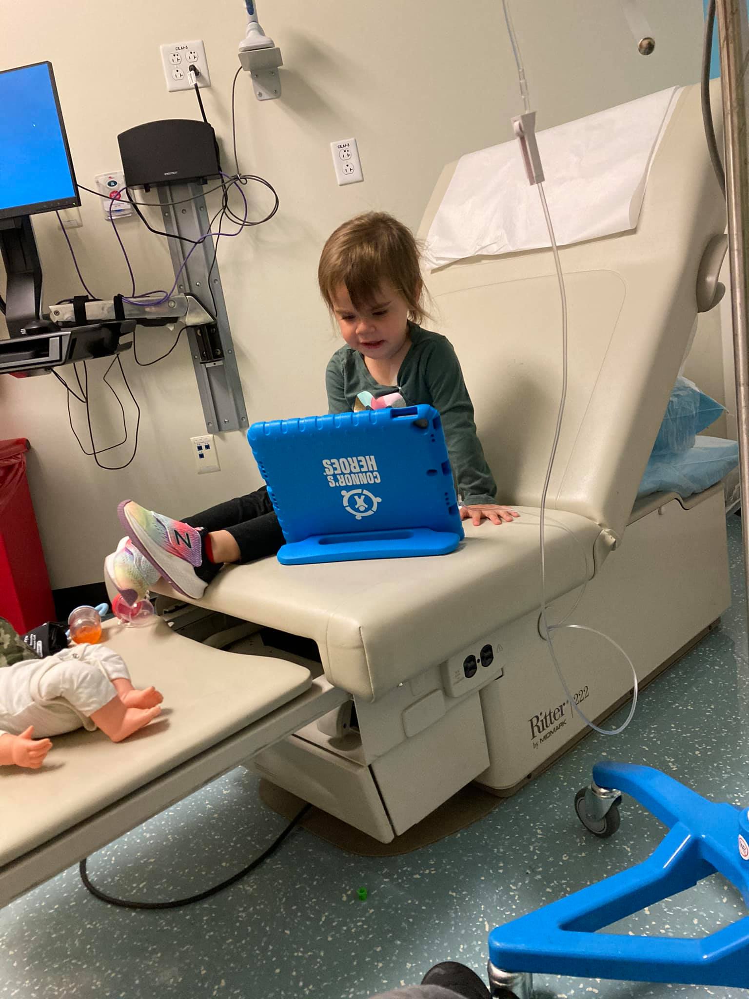 In a hospital room is a child looking at a tablet while getting an infusion