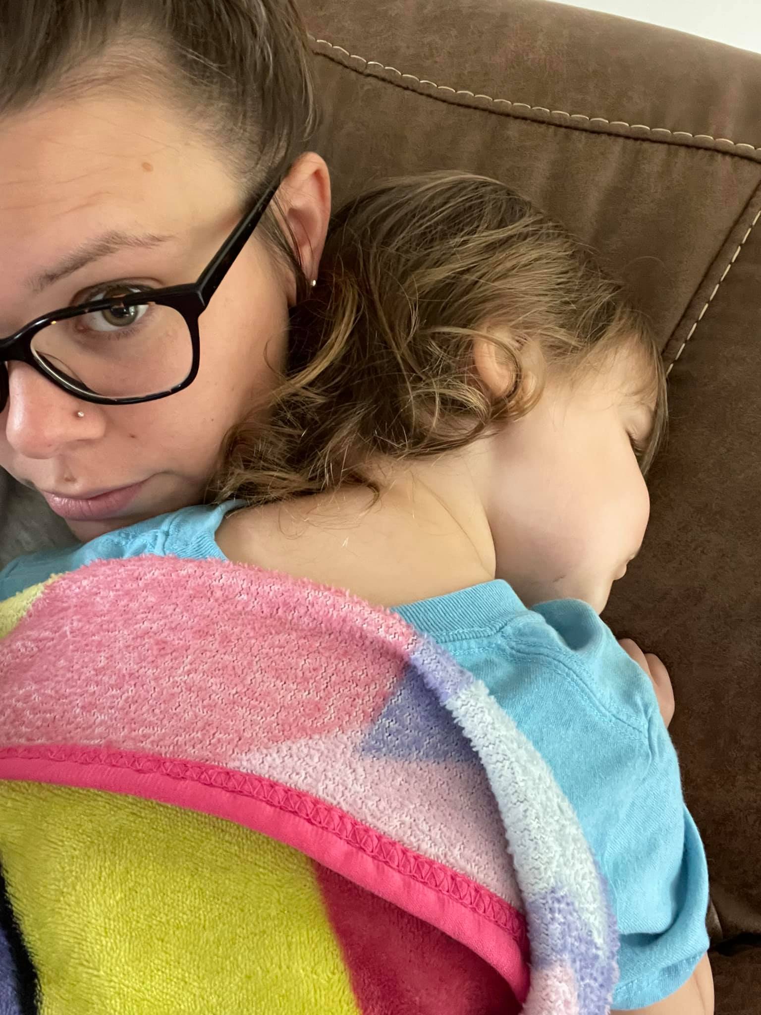 A mom wearing glasses and holding her daughter across her shoulder