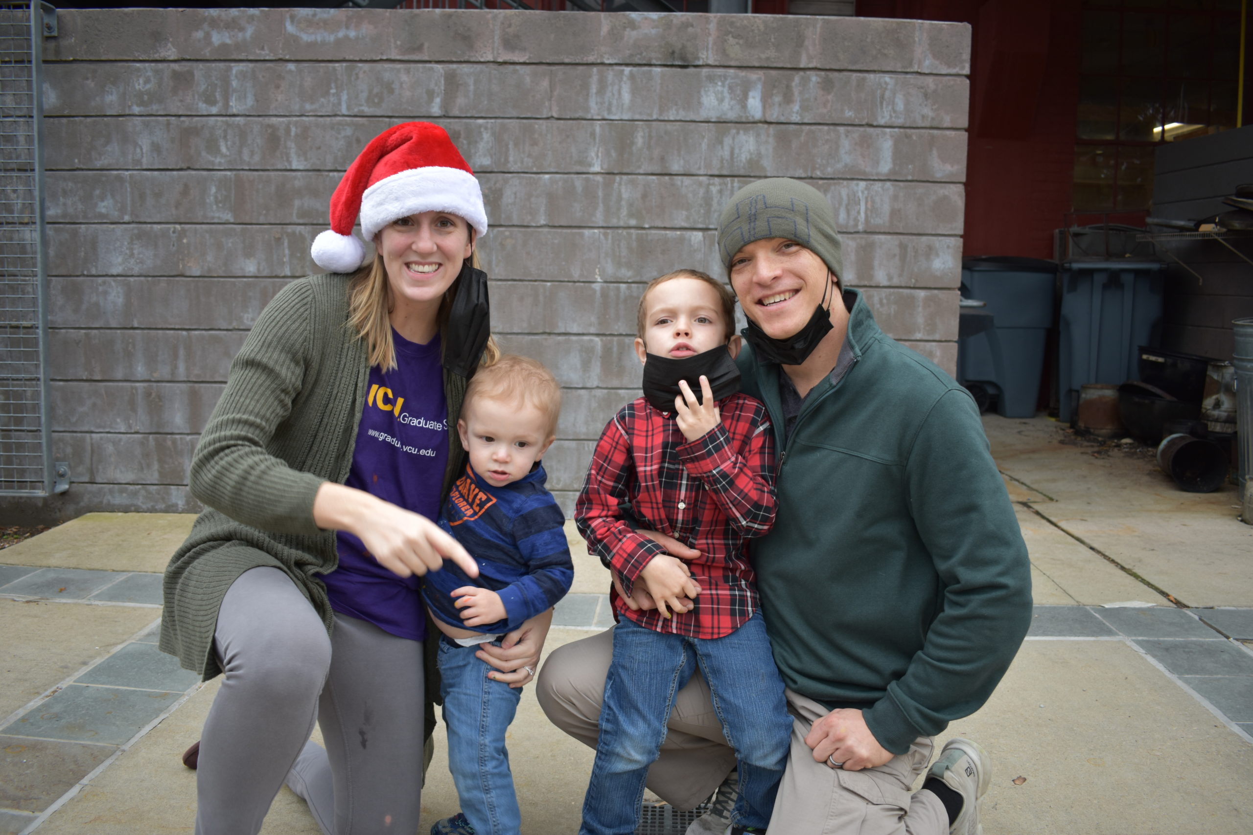 A mom and dad holding their two sons the parents are wearing santa hats