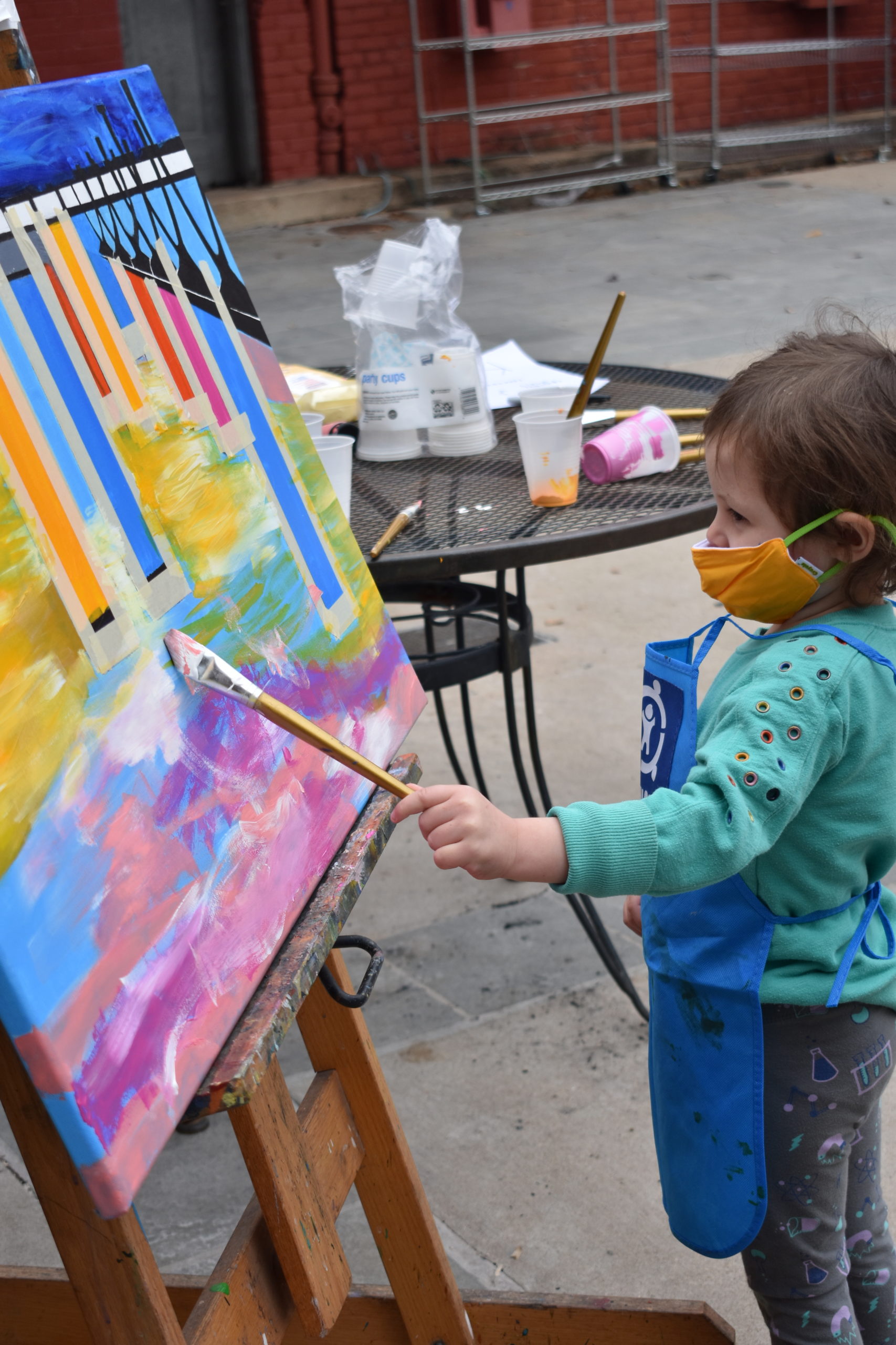 A girl holding a paint brush and painting on a large canvas