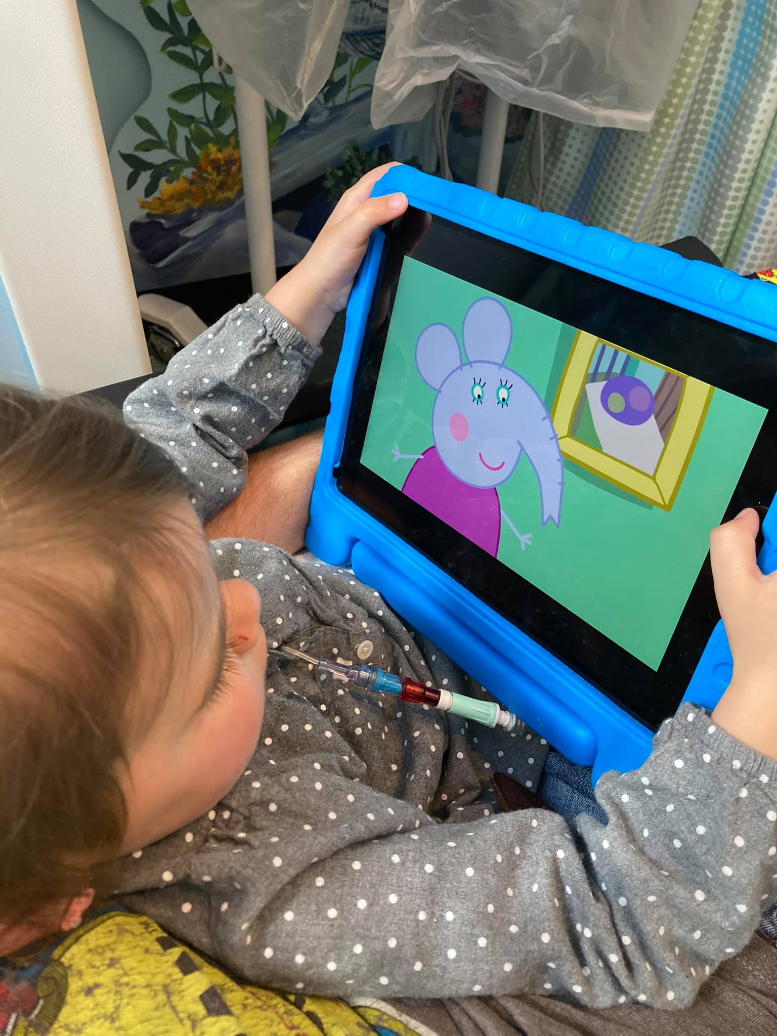 Child sitting on a hospital bed watching a cartoon on her ipad
