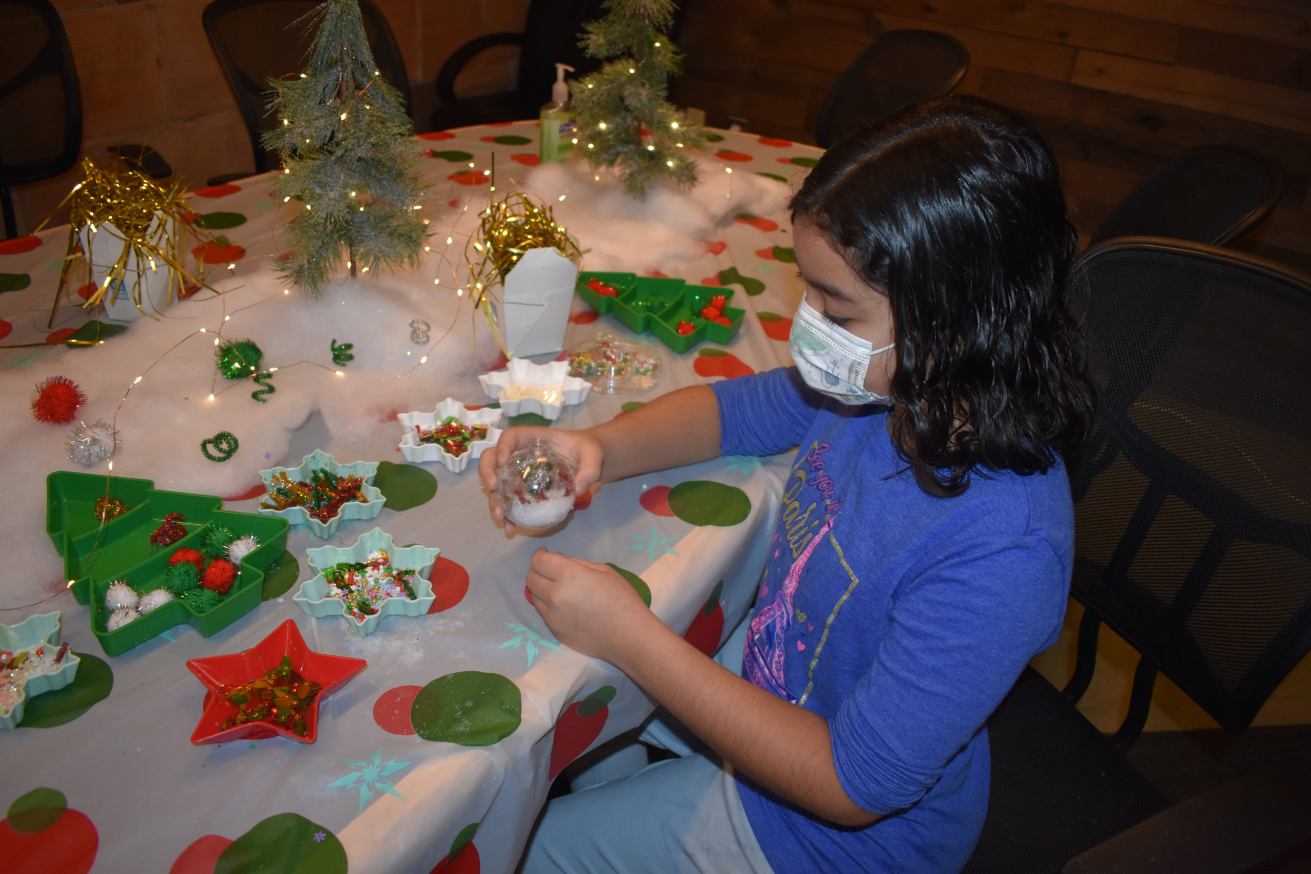 A girl sitting at a table making a craft at a holiday party