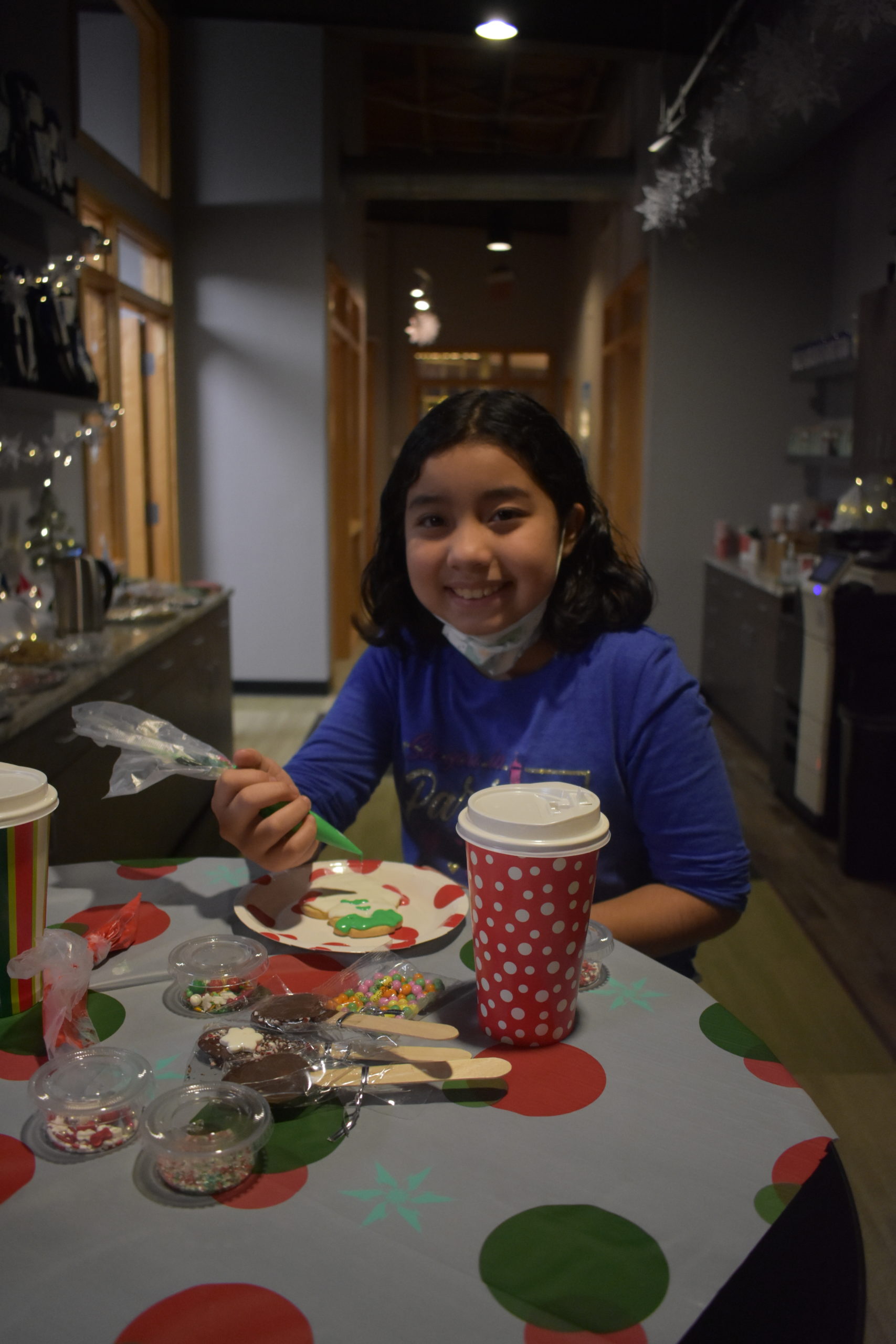 A girl sitting at a table making a craft at a holiday party