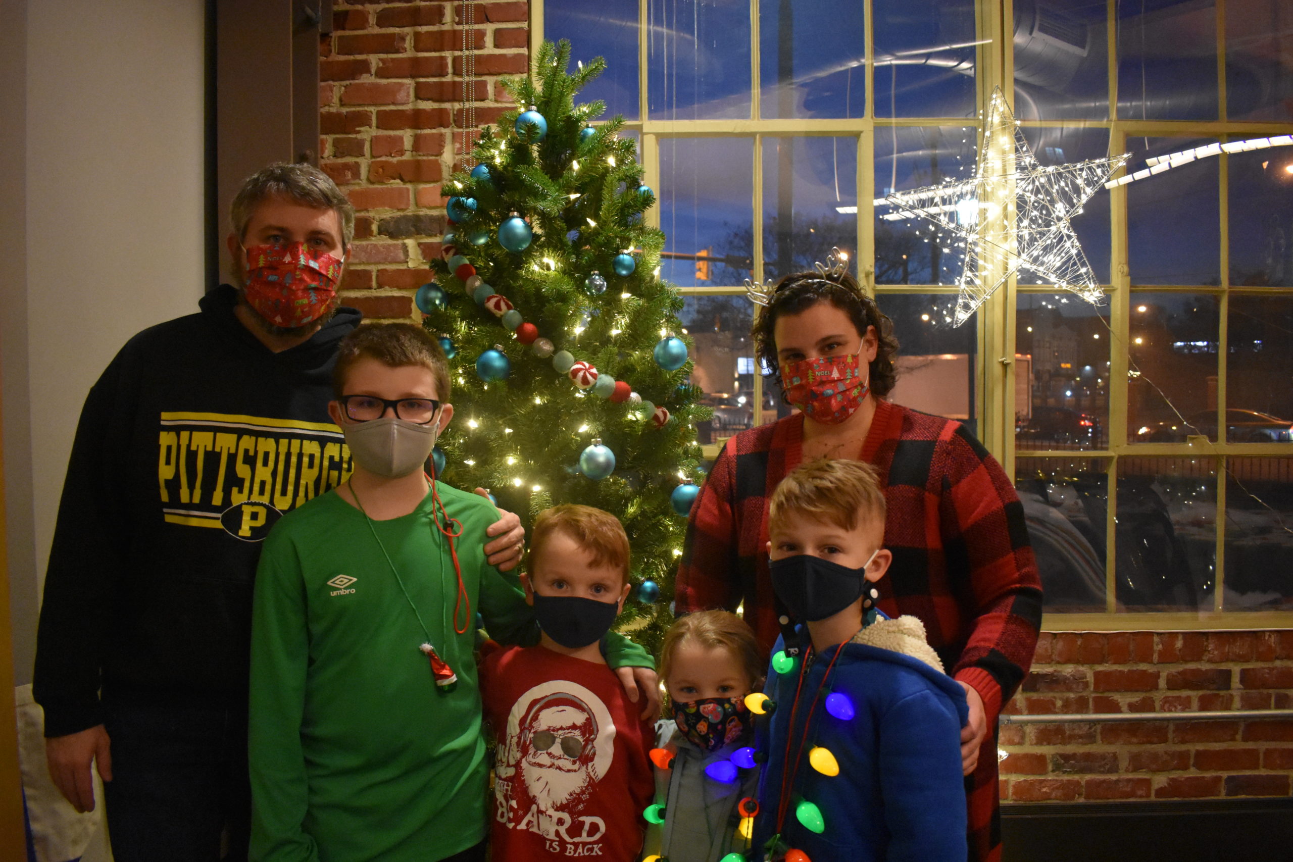 Parents standing with their three children in front of a tree decorated for the holidays