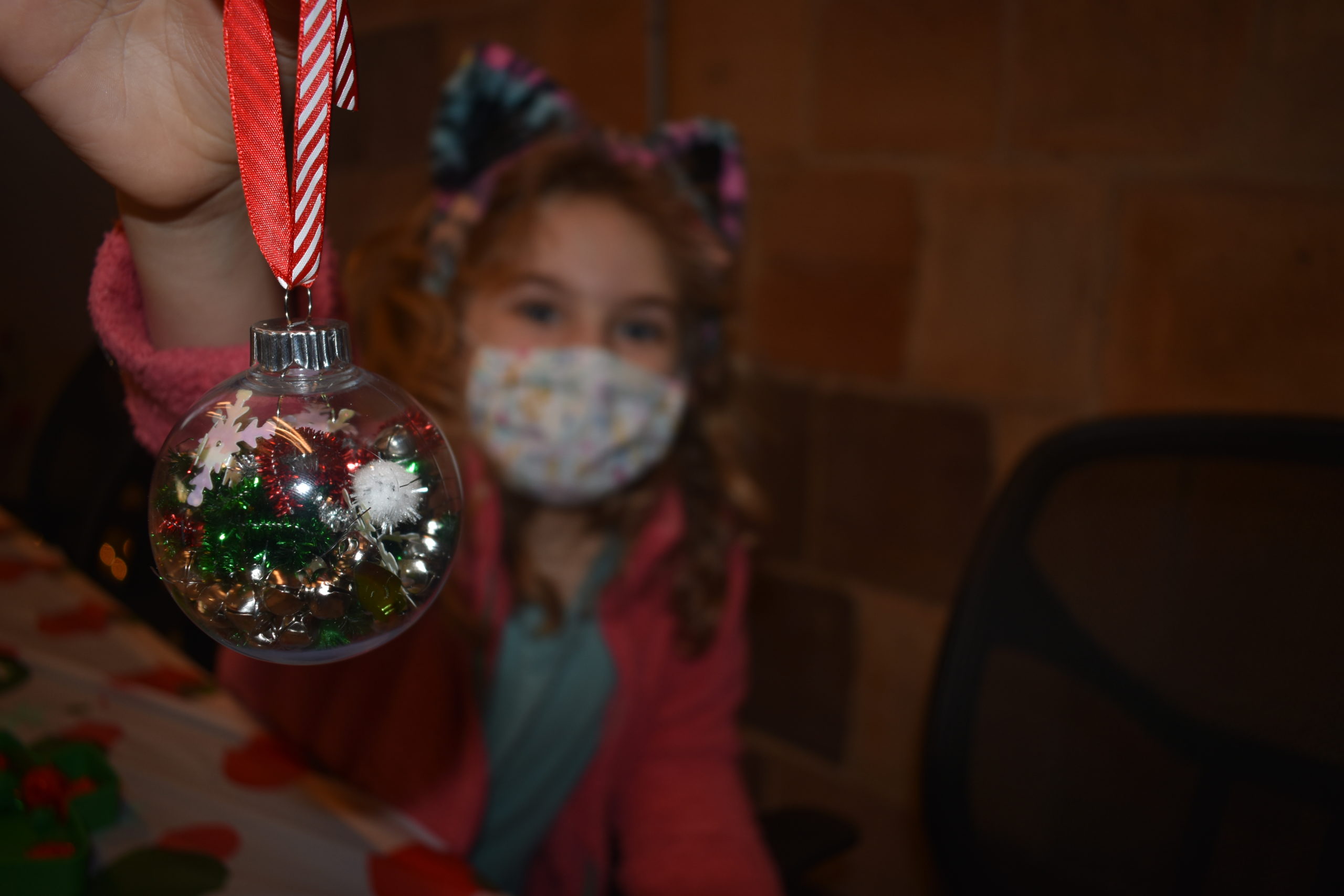 A girl holds up an ornament she made at a holiday party