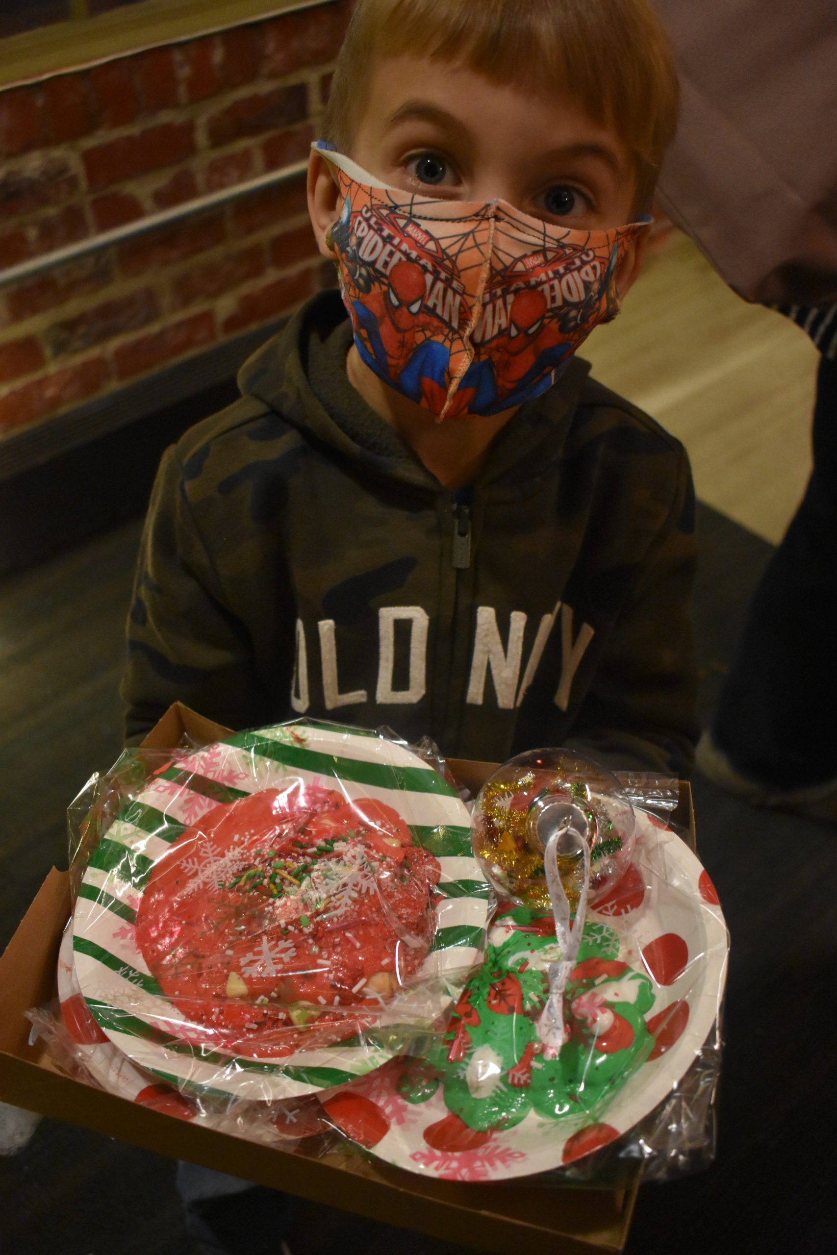 A boy holds two plates with cookies decorated with lots of icing and sprinkles