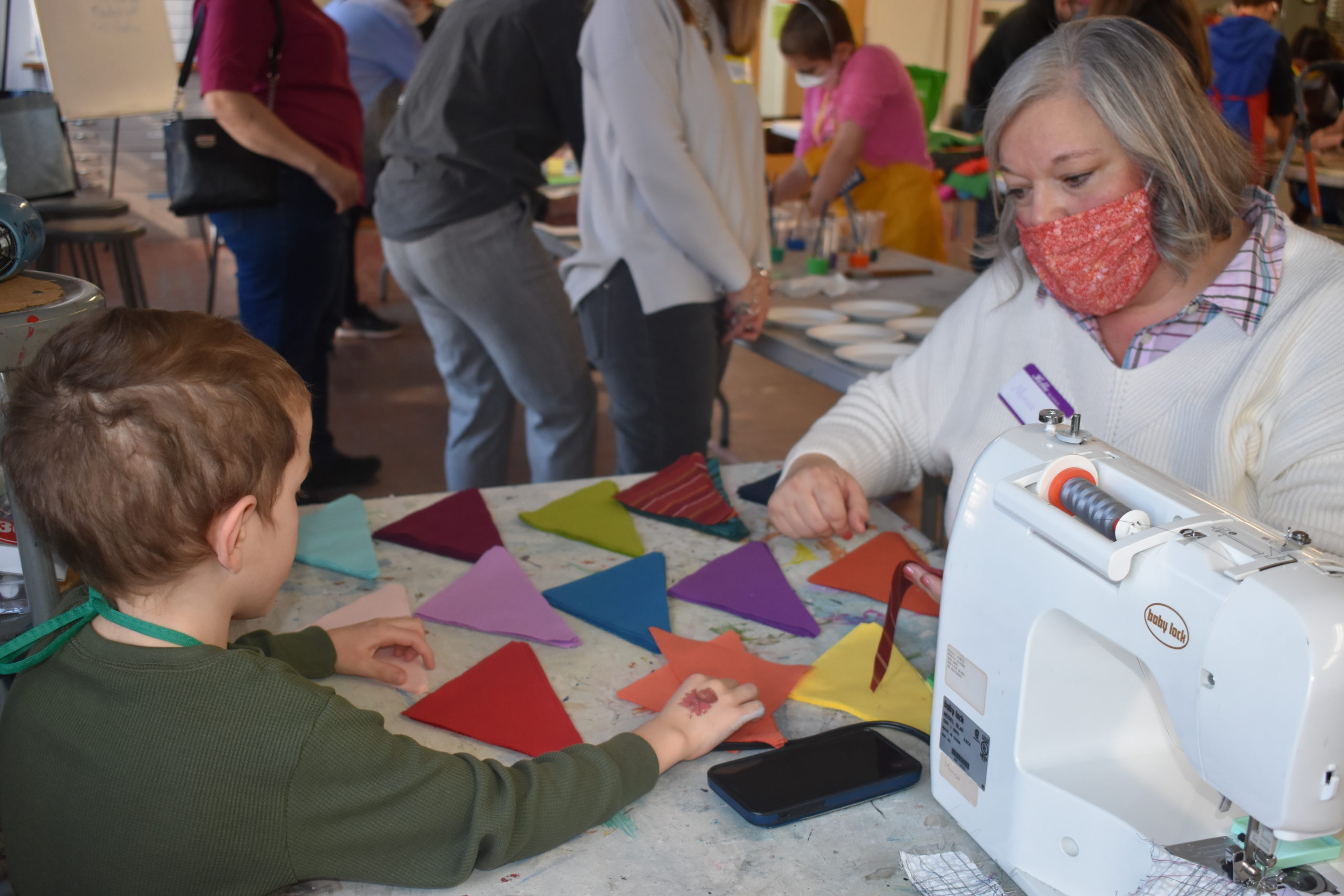 A woman showing a child how to piece together a quilt on a sewing machine