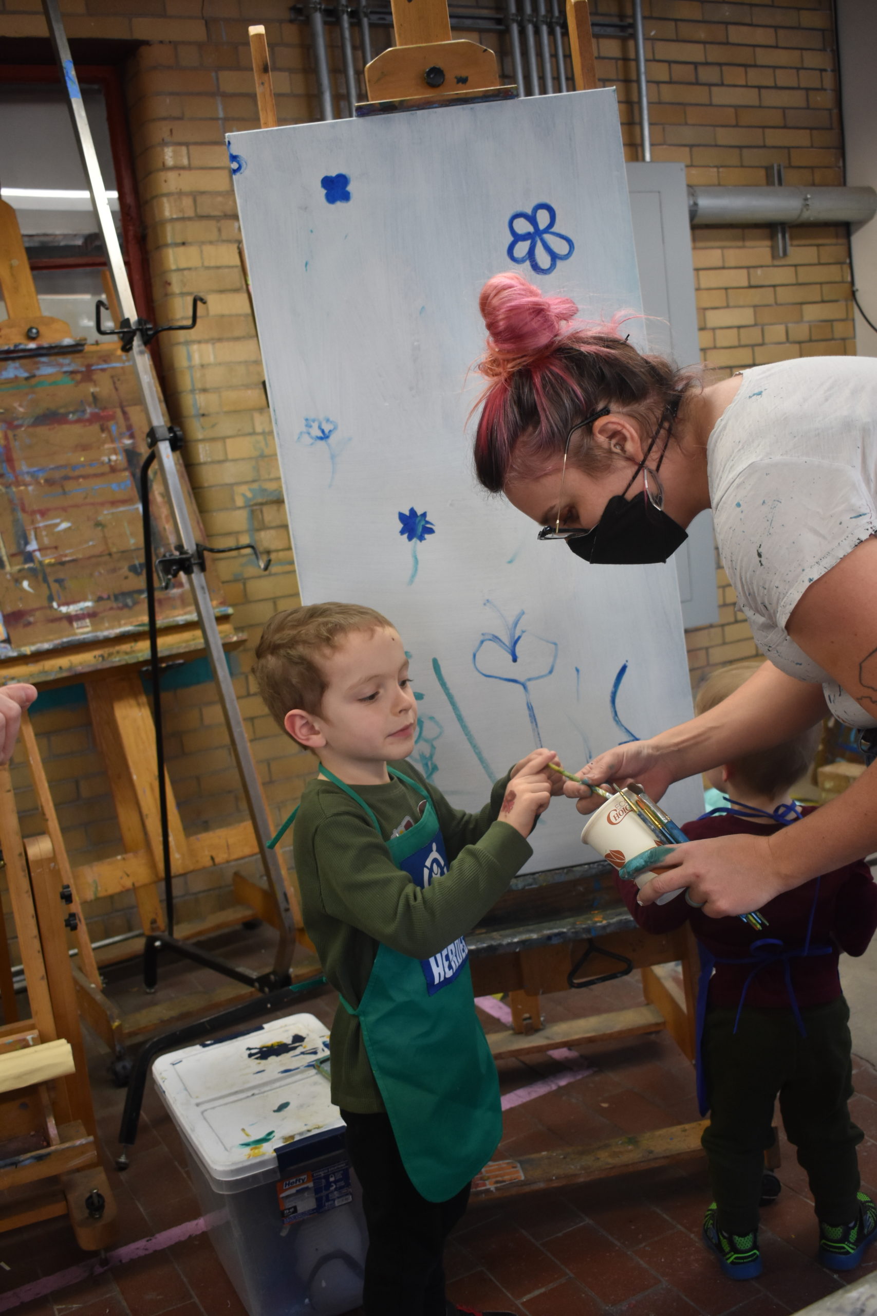 A child helping an artist paint on a large canvas