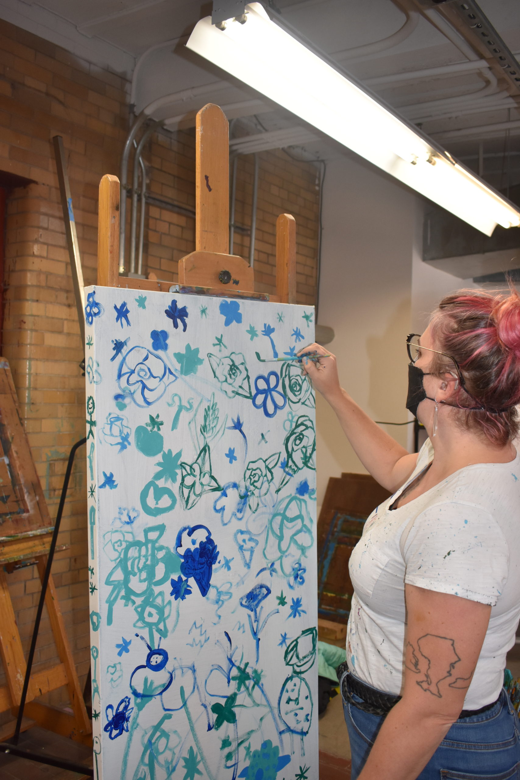 An artist painting blue and green outlines on a large canvas