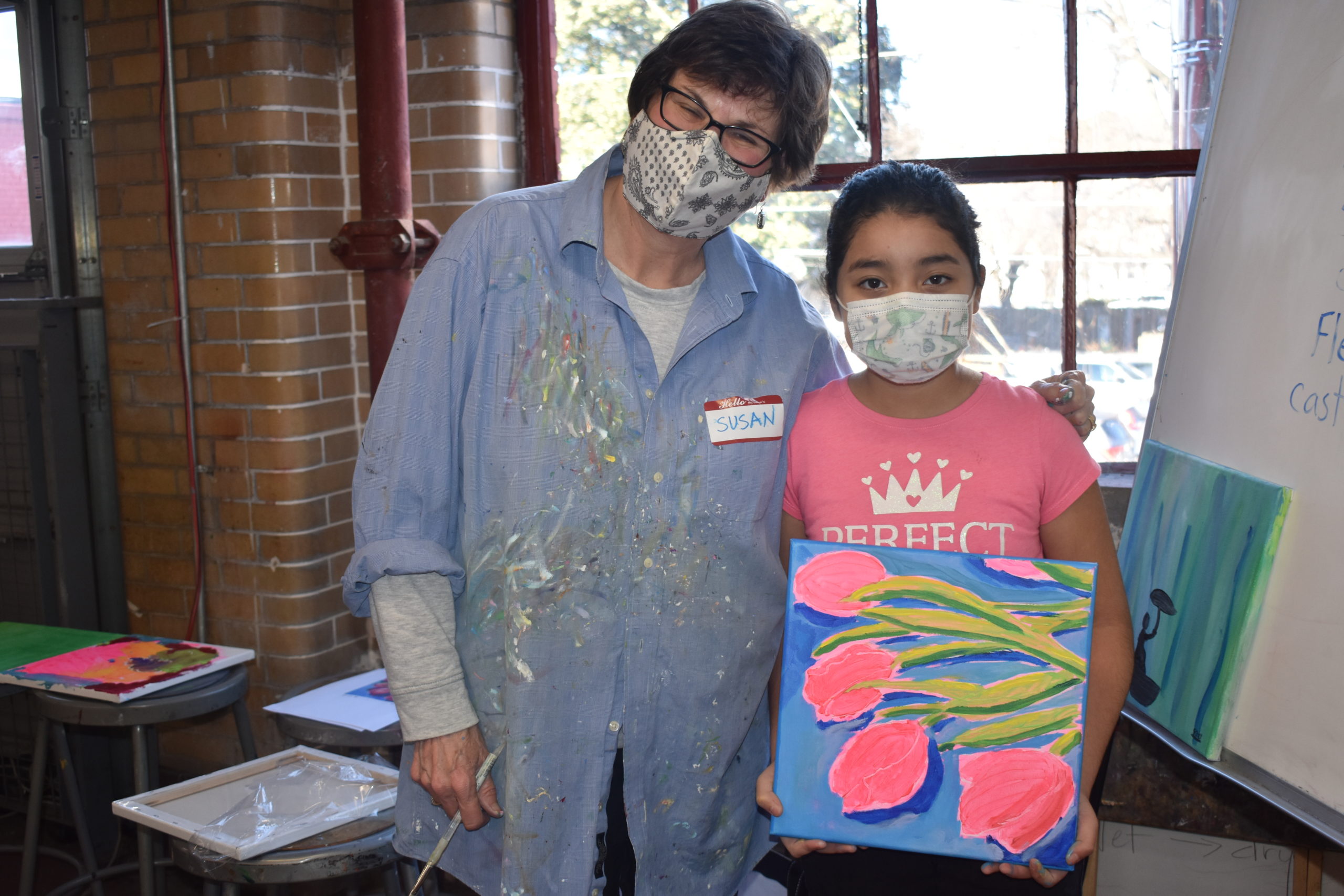 A woman standing next to a child who is holding a painting of pink tulips