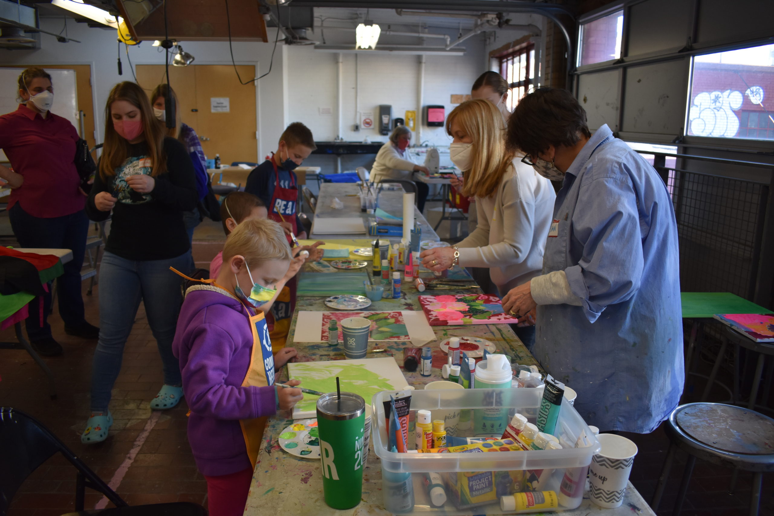 A group of children and adults in an art studio working on paintings