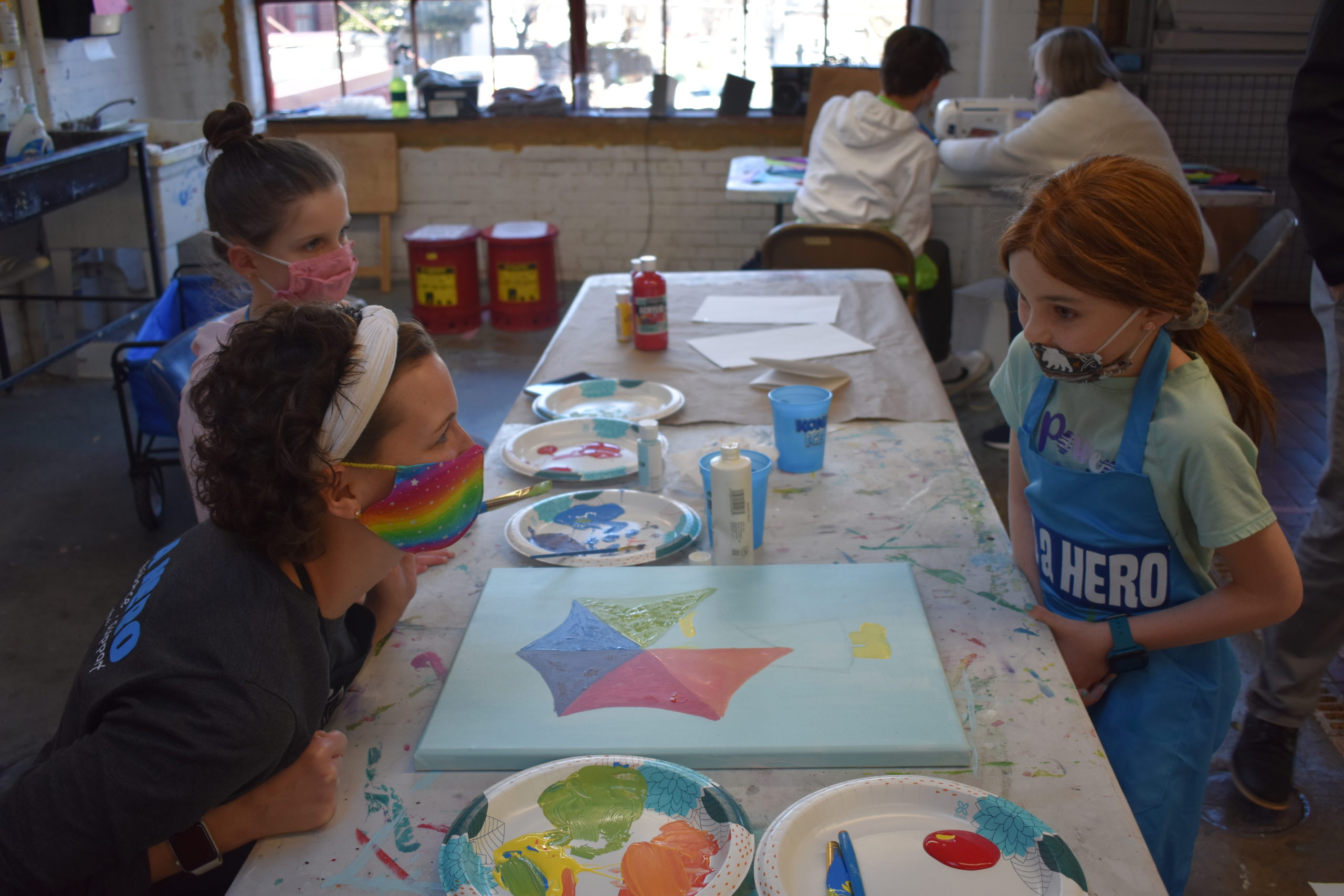 Two children in an art studio working with an adult on a painting