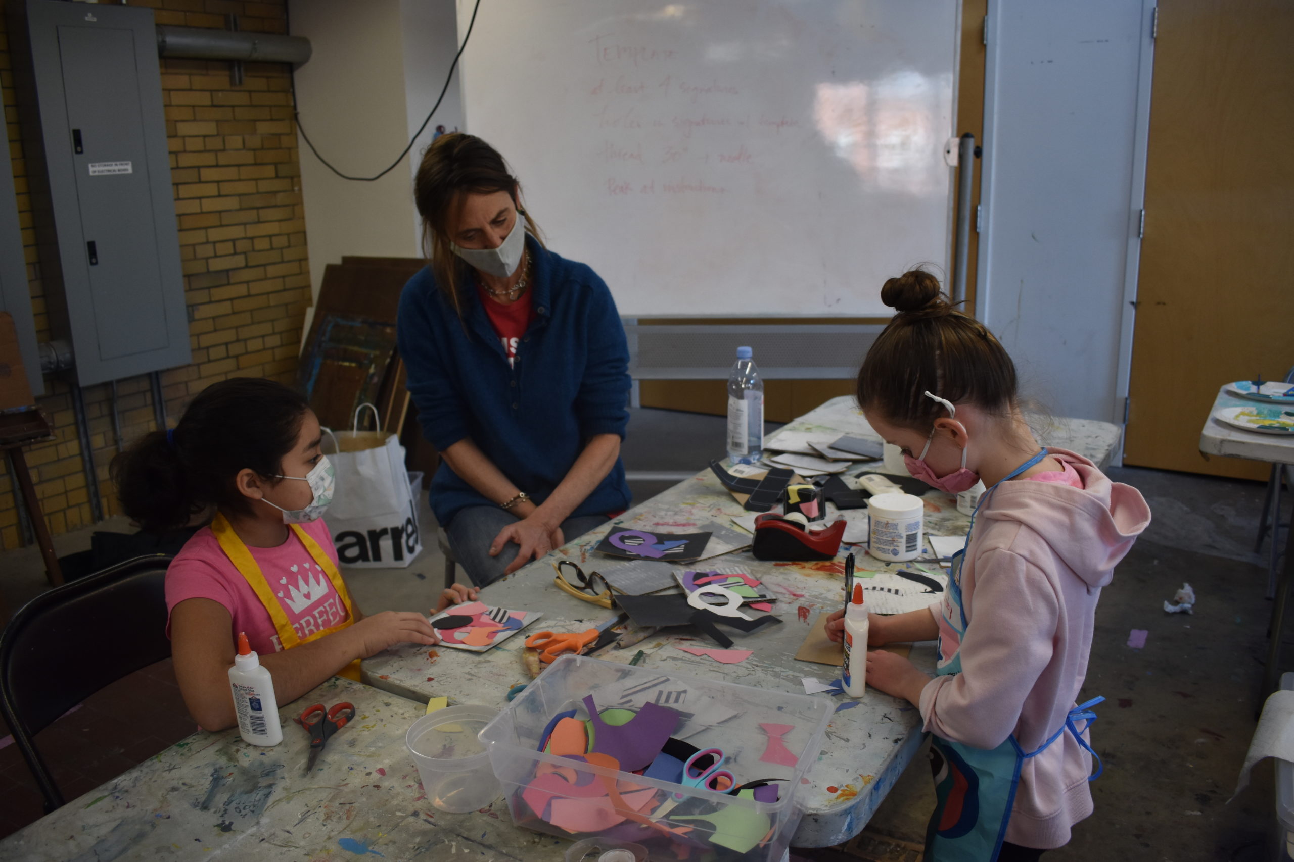 Two children in an art studio working with an adult on a craft project