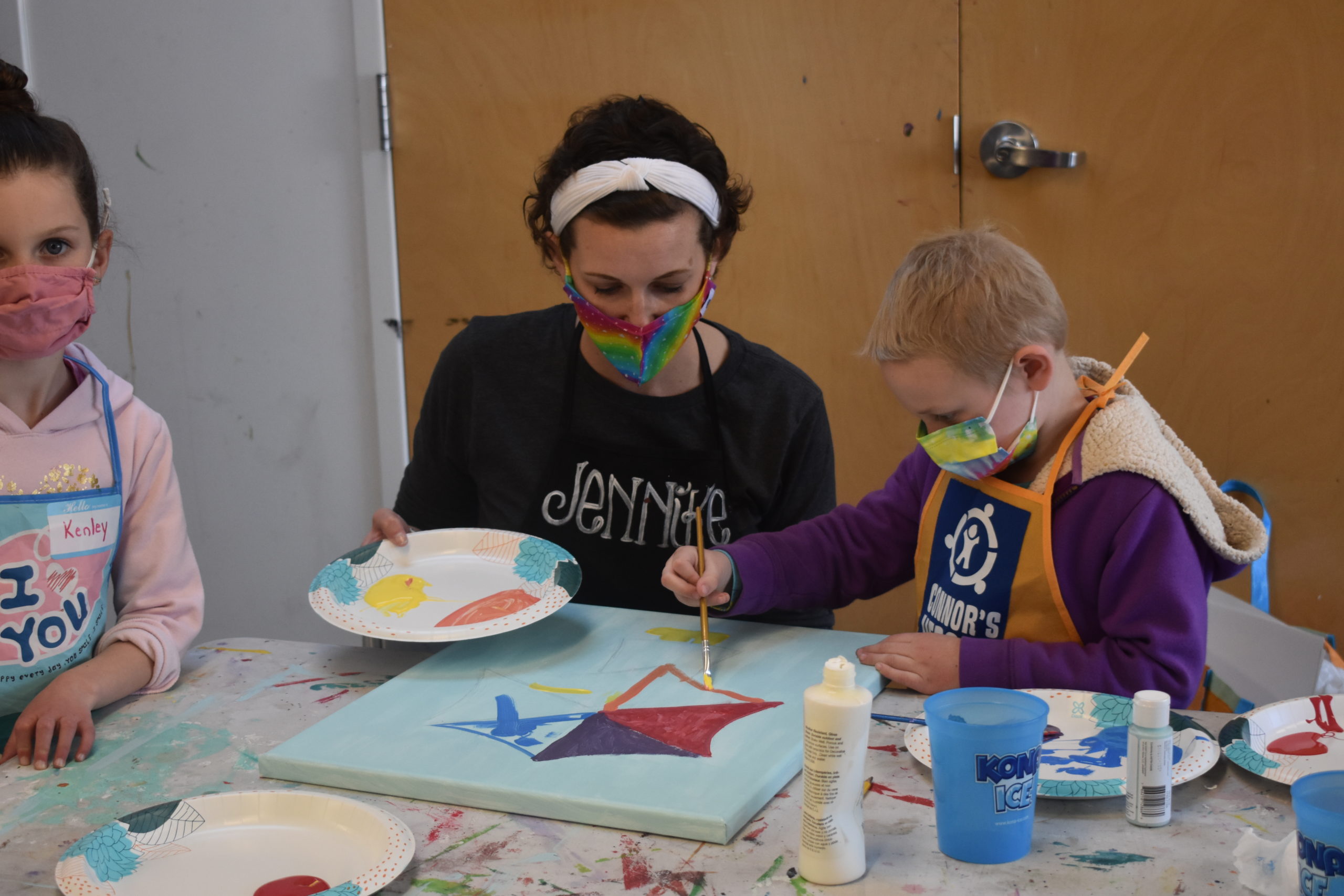A child in an art studio painting on a canvas with an adult helping her