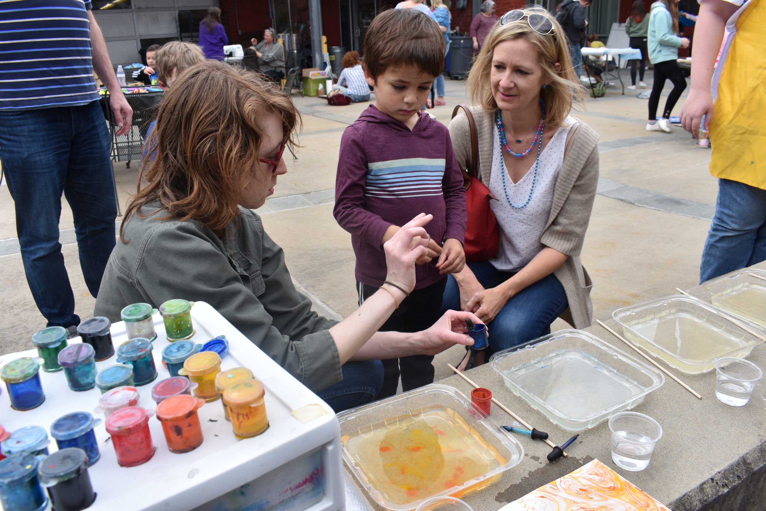 A woman is showing a child and his parent how to drip paint