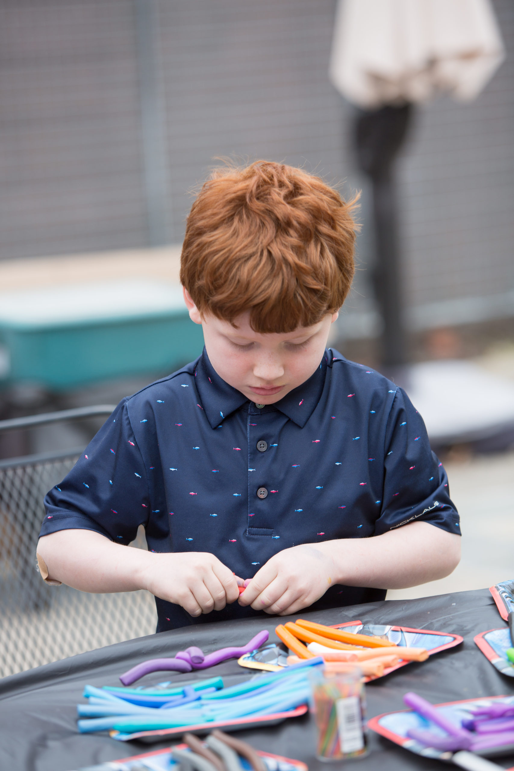A boy is outdoors at a table molding pieces of clay