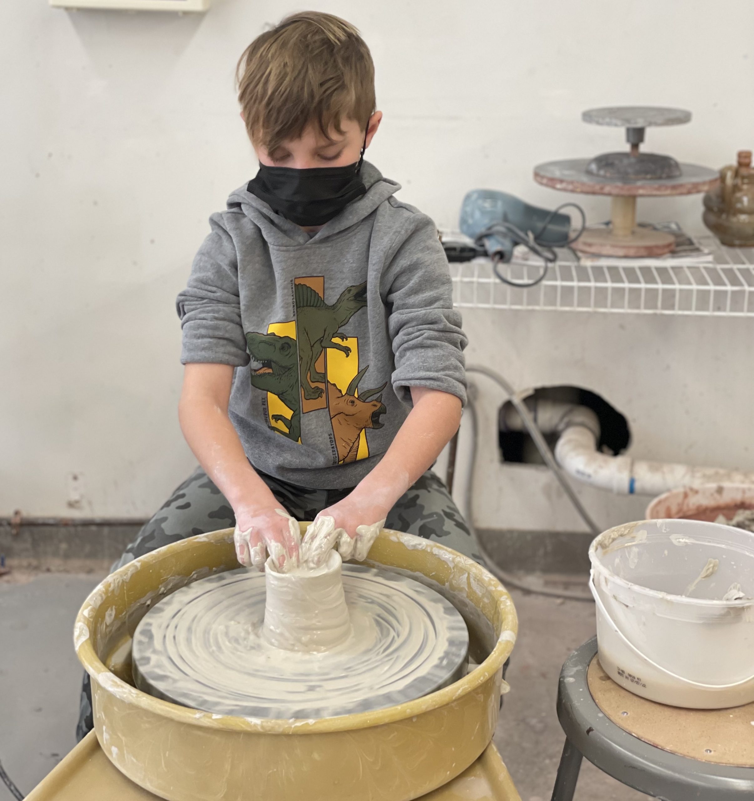 A child sitting at a pottery wheel shaping a piece of clay